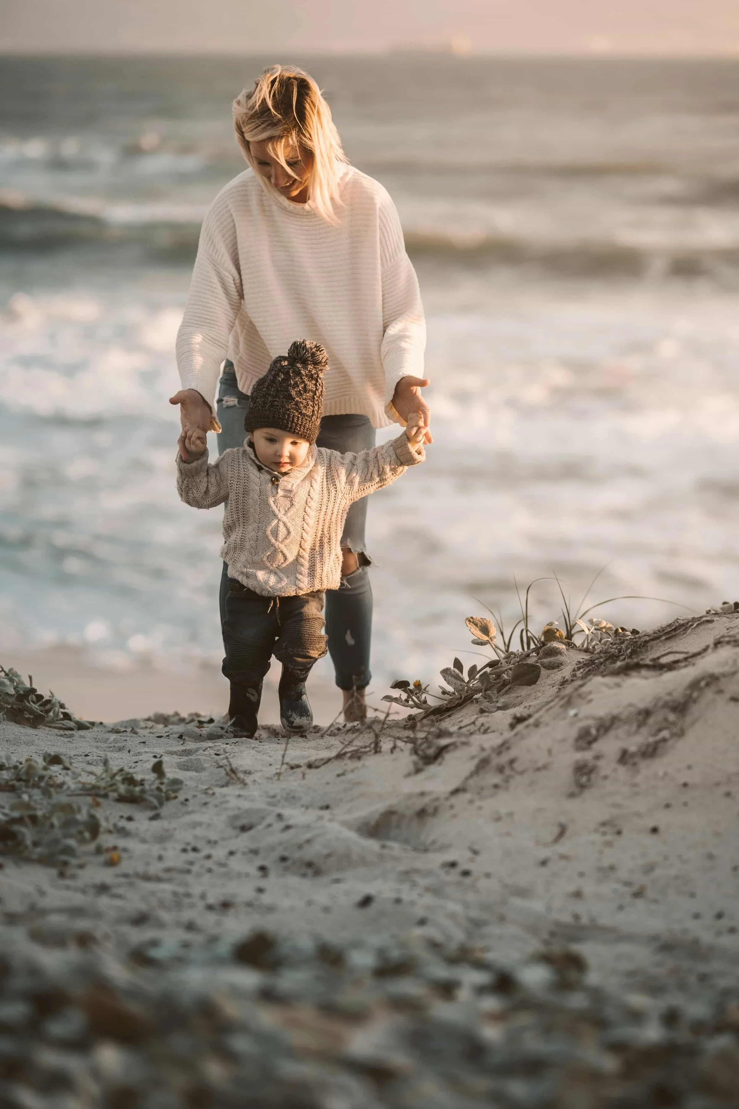 mom walking with toddler on beach at sunset