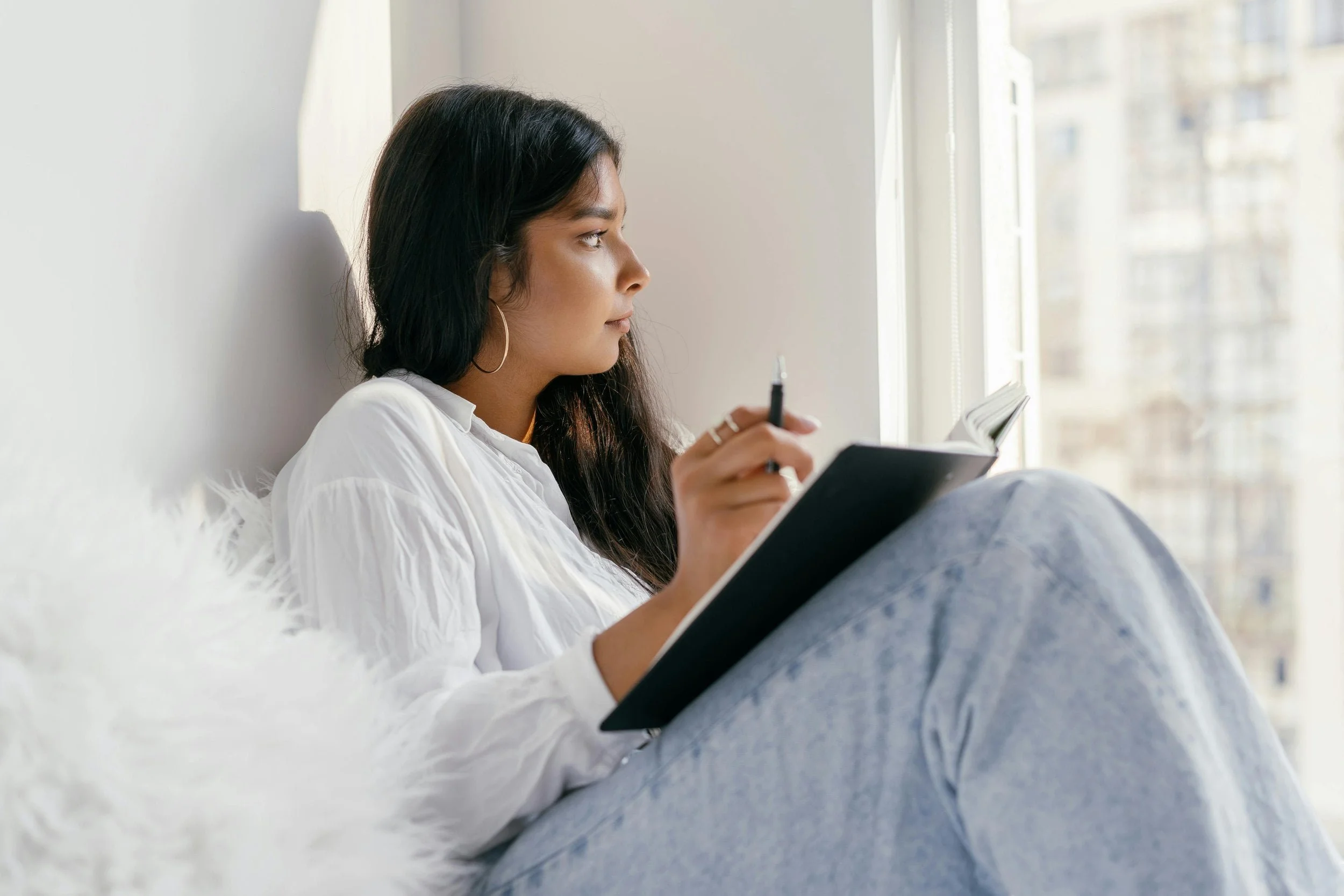 Woman journaling while looking out window with fuzzy pillow