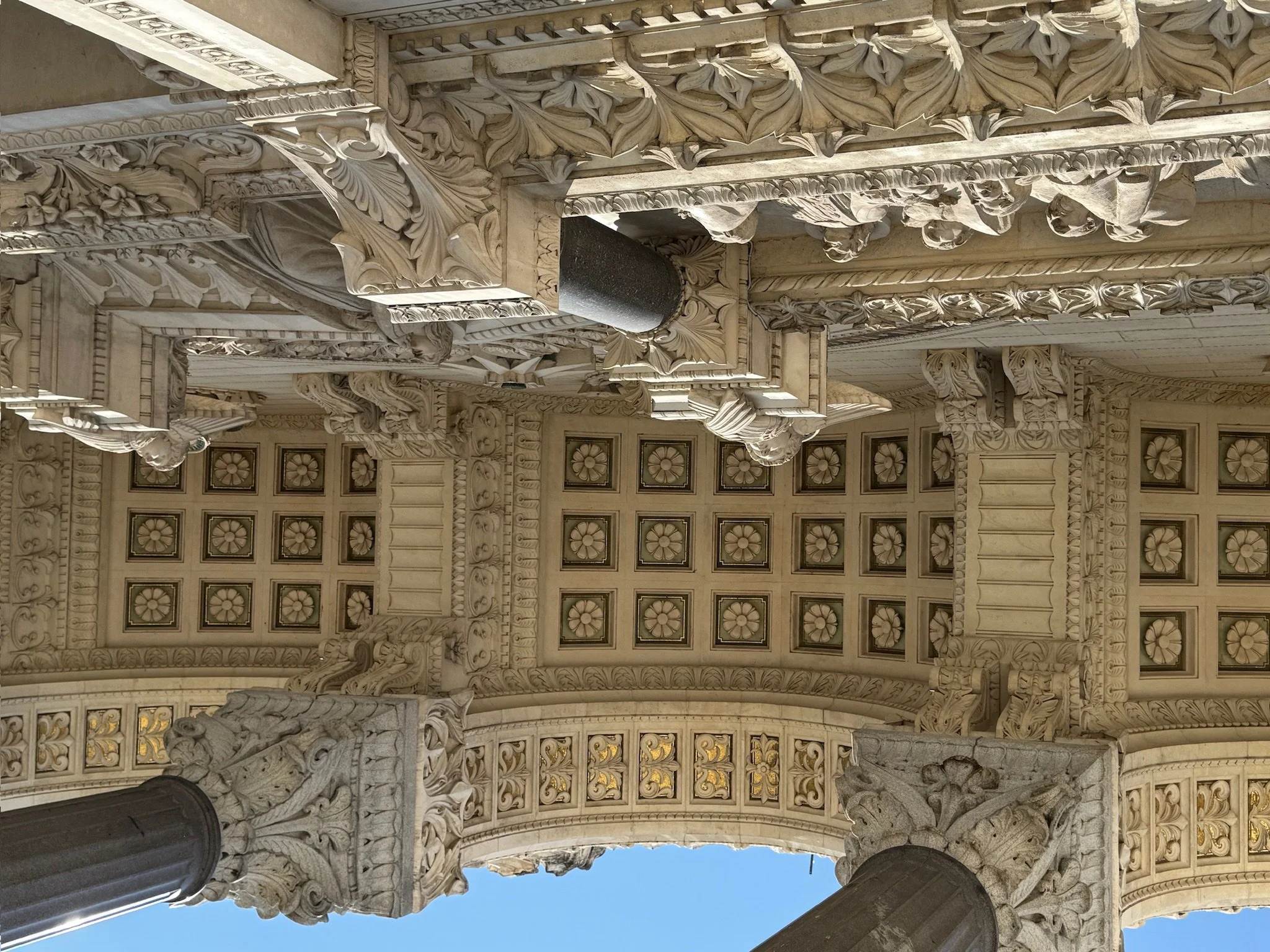Intricate white marble carvings and sculptures on a ceiling, featuring floral patterns, scrollwork, and detailed decorative elements.