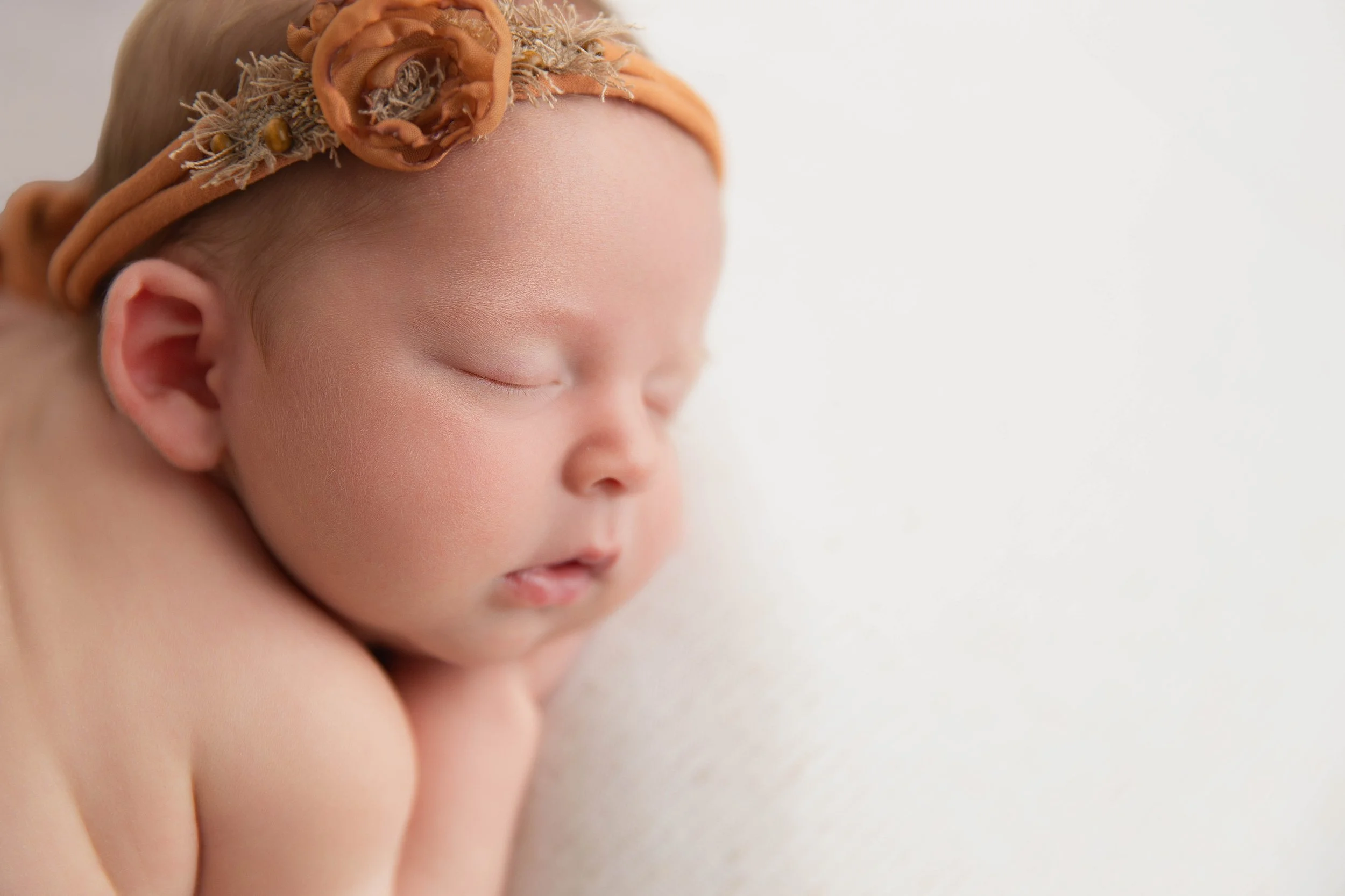 Close-up of a sleeping baby with a floral headband resting on a soft surface.