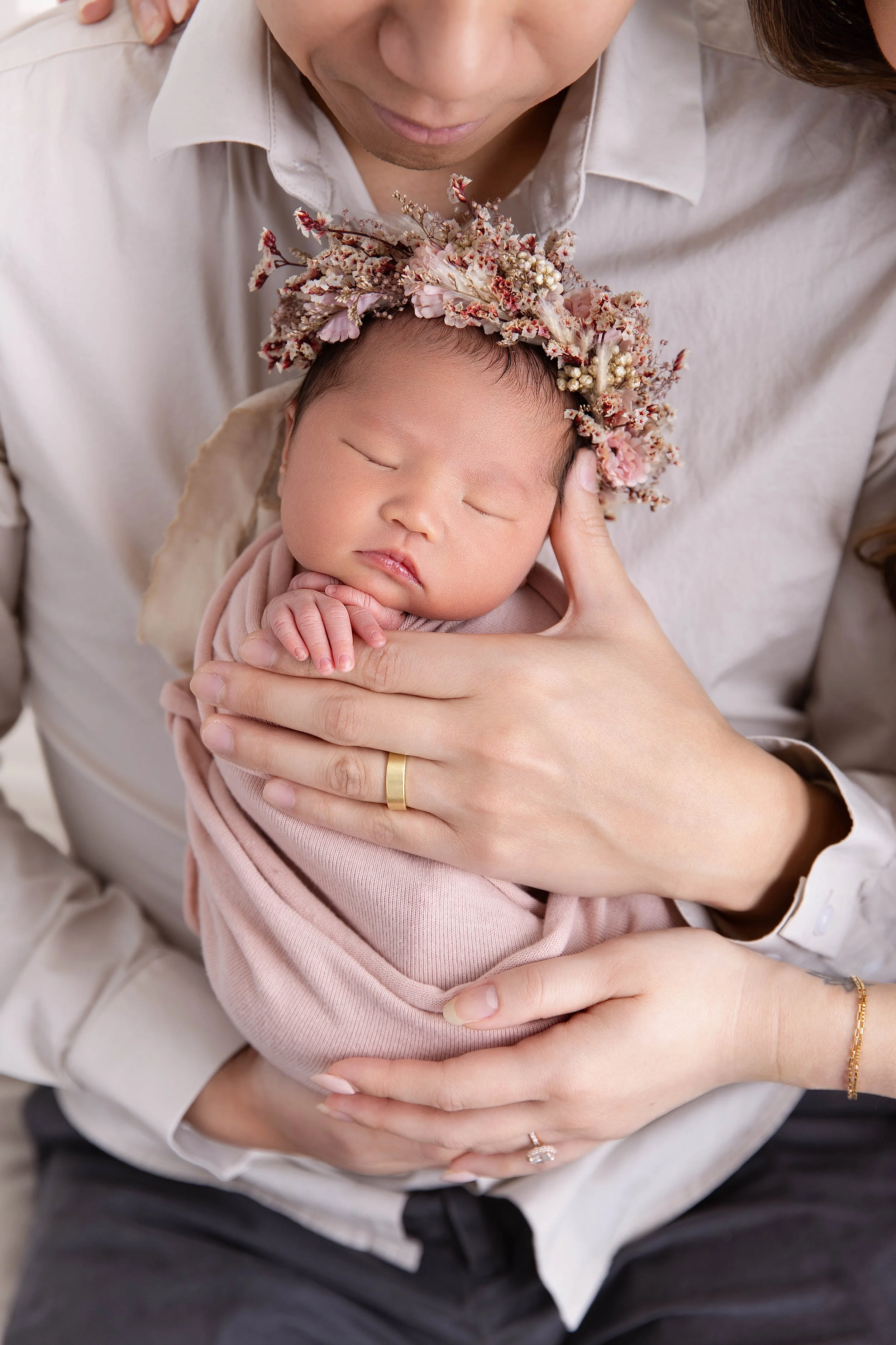 A sleeping baby with a floral headband, cradled in an adult's arms, against a neutral background.