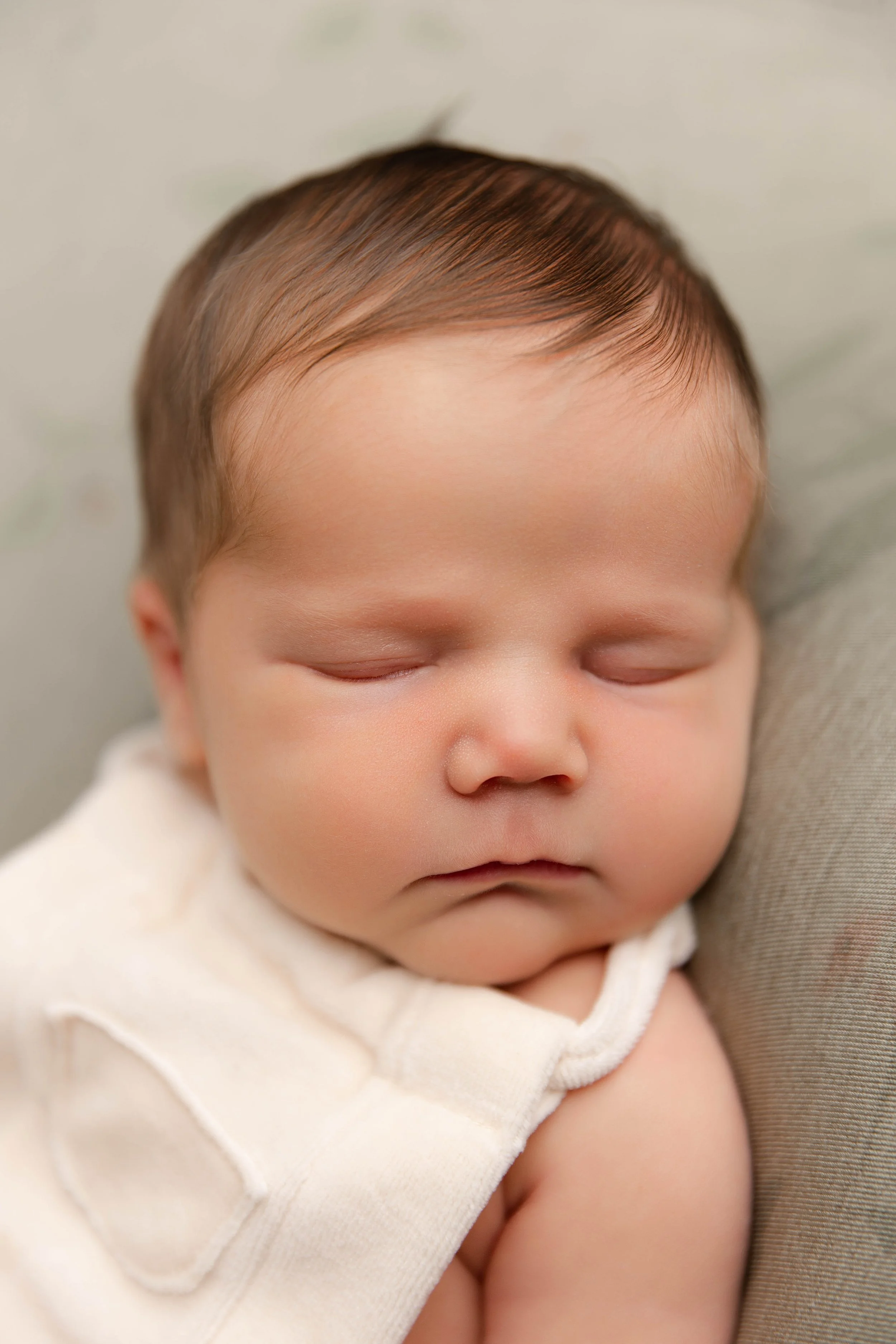 Close-up of a sleeping baby with smooth skin and light brown hair, resting on a soft surface.