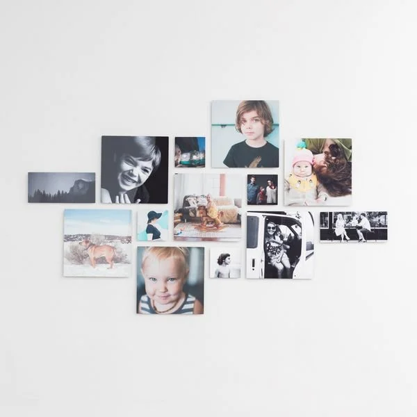 A collection of various photographs and picture prints arranged on a white wall, including portraits of children, animals, landscapes, and candid moments.