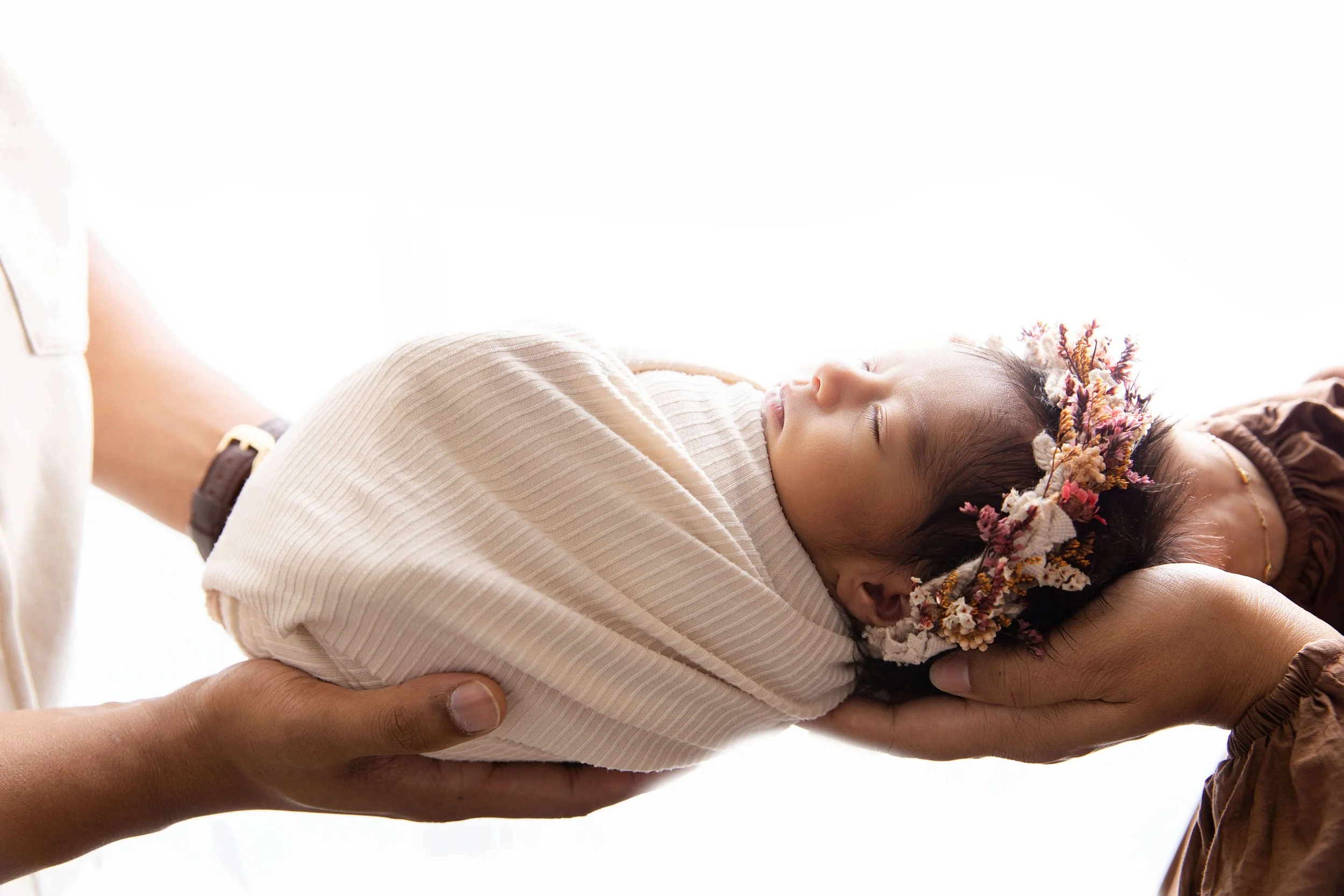 swaddled baby held by parents' hands