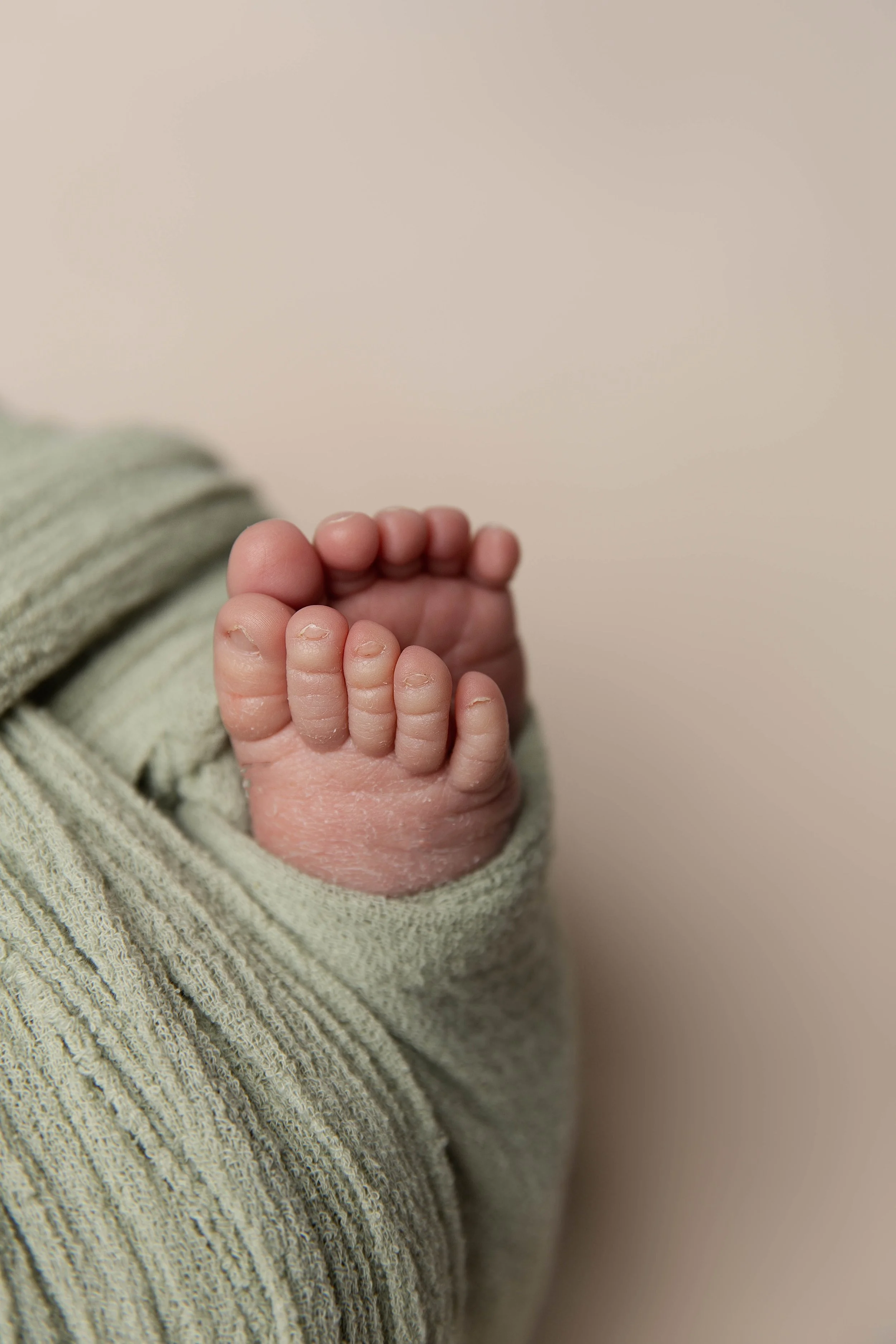 Close-up of a newborn baby's feet wrapped in a soft, striped green blanket.