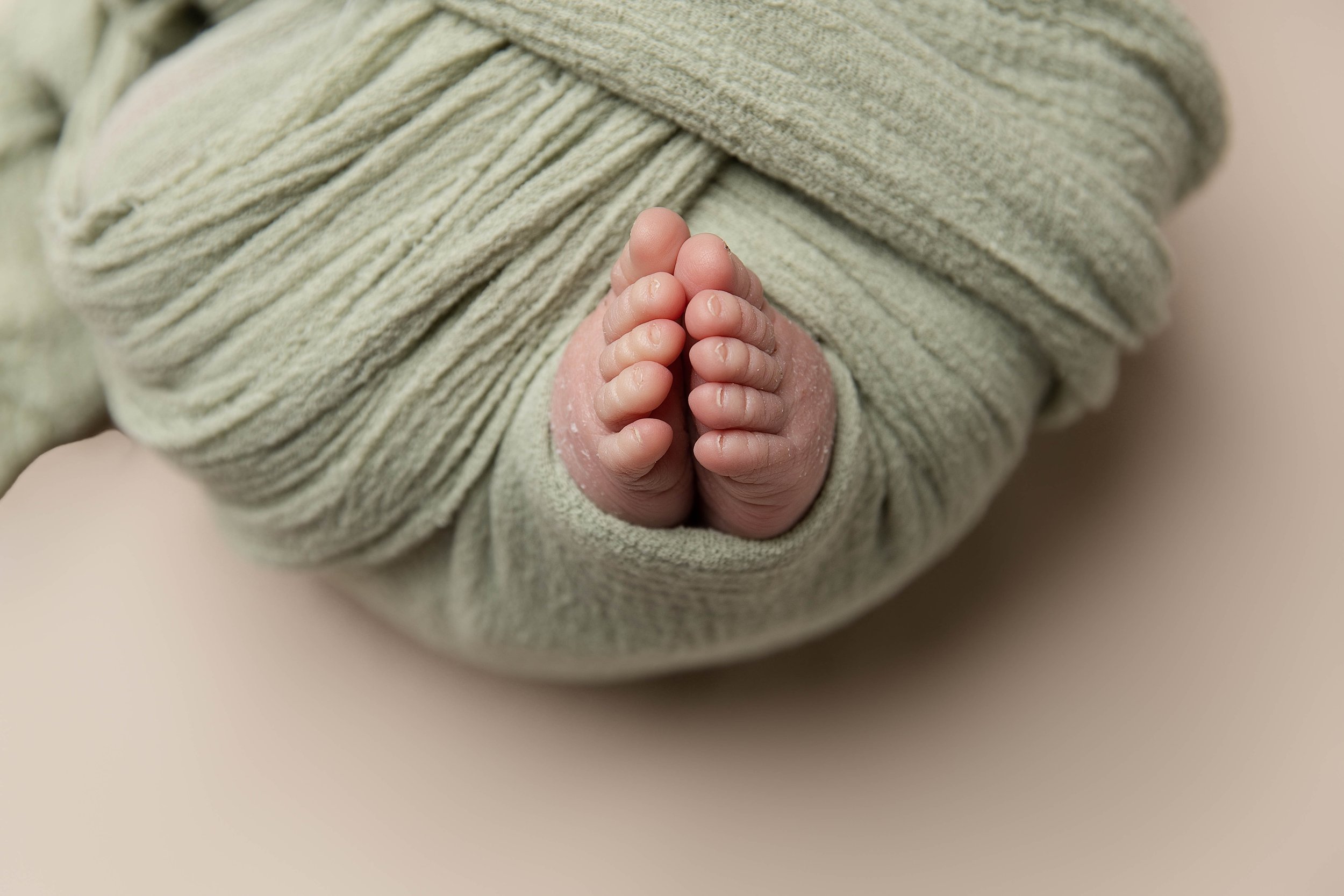 Close-up of a newborn baby's feet wrapped in light green fabric with the toes visible.