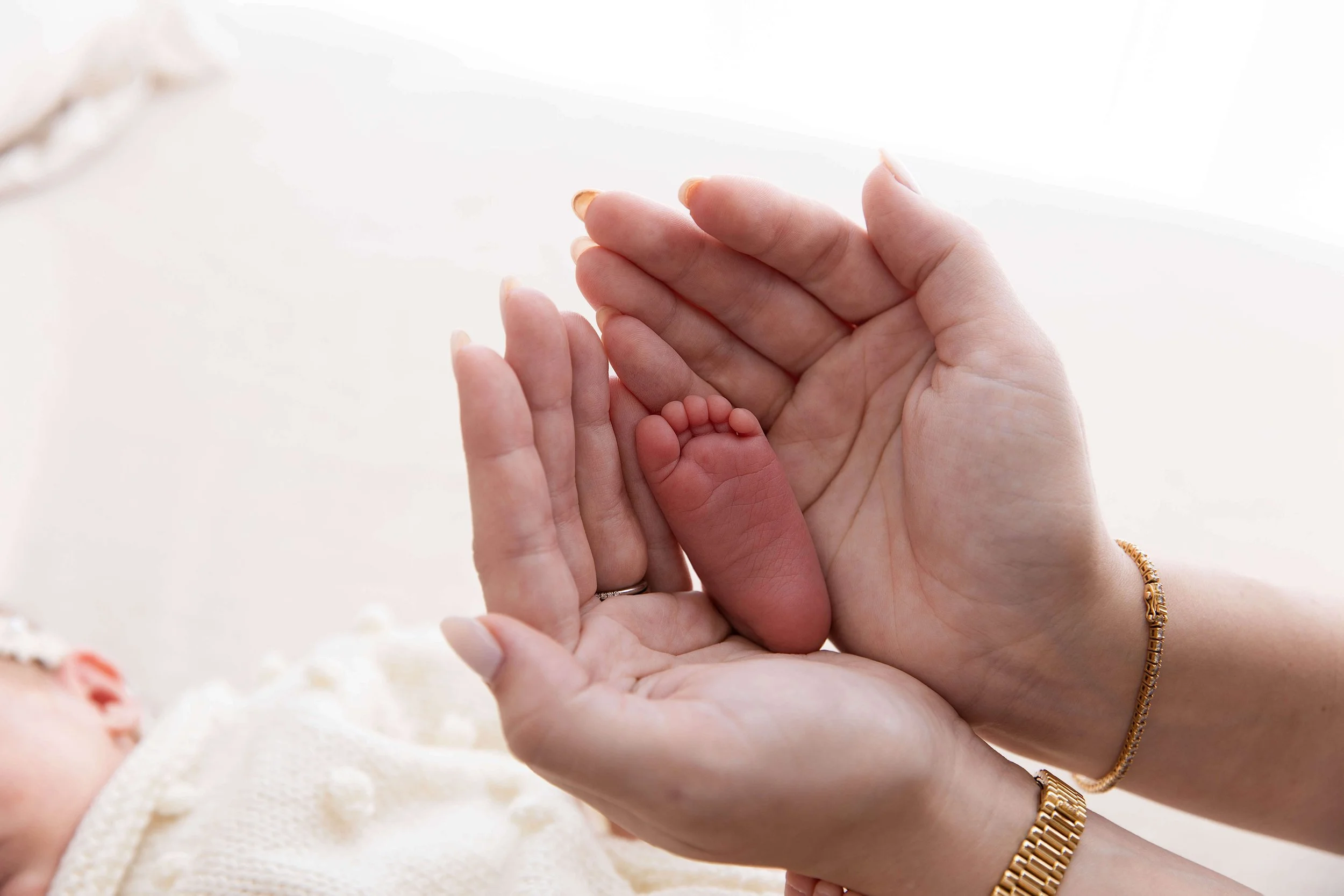 Close-up of adult hands gently holding a newborn baby's tiny hand, with a blurred background.