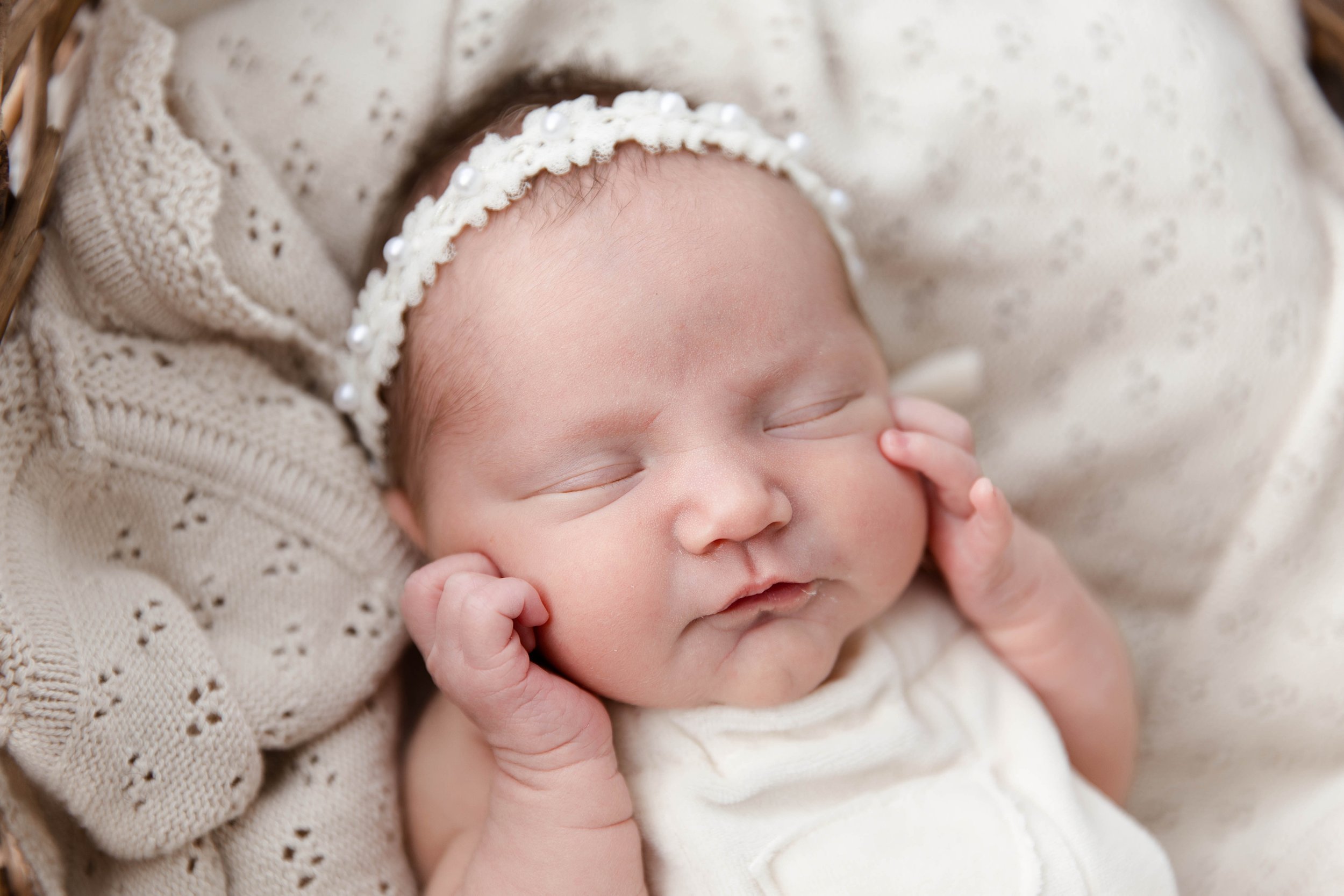 Close-up of a sleeping baby with a knitted bonnet, resting on a soft cream blanket.