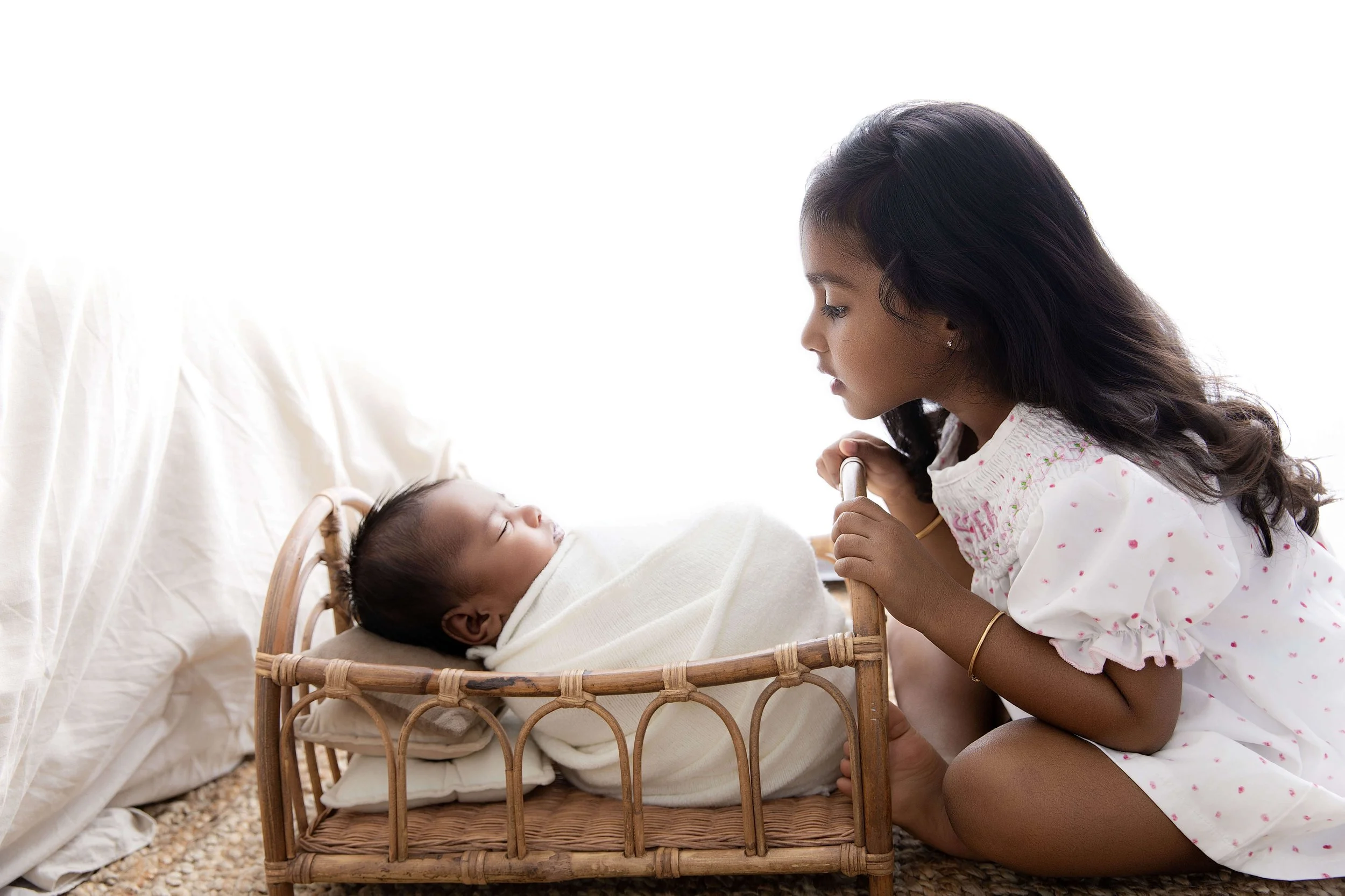 older sister looking down at baby brother in a basket