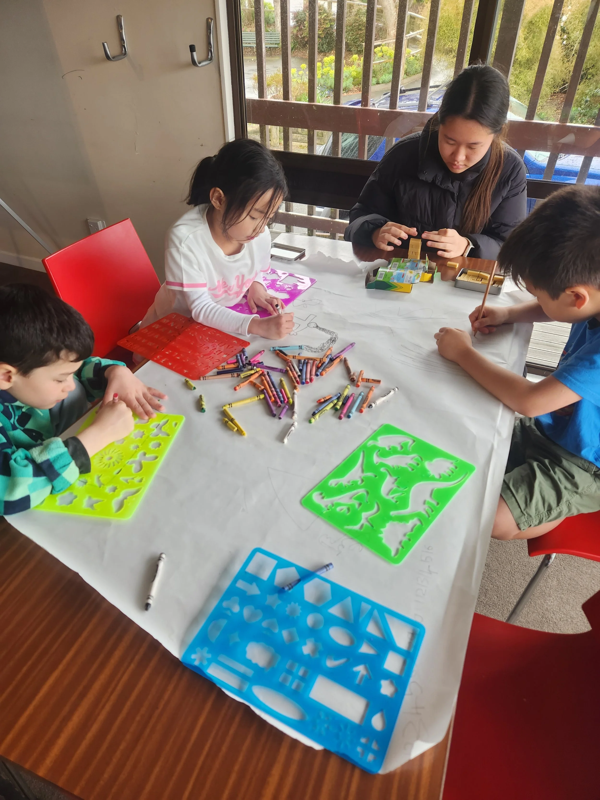 Children and an adult sitting around a table using stencils, crayons, and drawing.