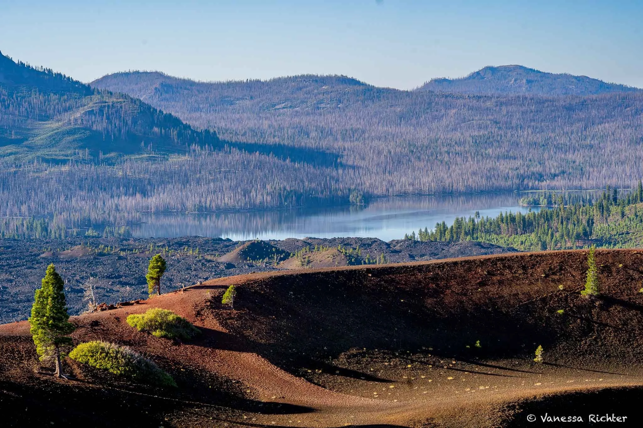 90mm view from the rim of Cinder Cone in Lassen Volcanic National Park looking toward Snag Lake, with the lake's blue water appearing closer than it actually is against the surrounding forest.