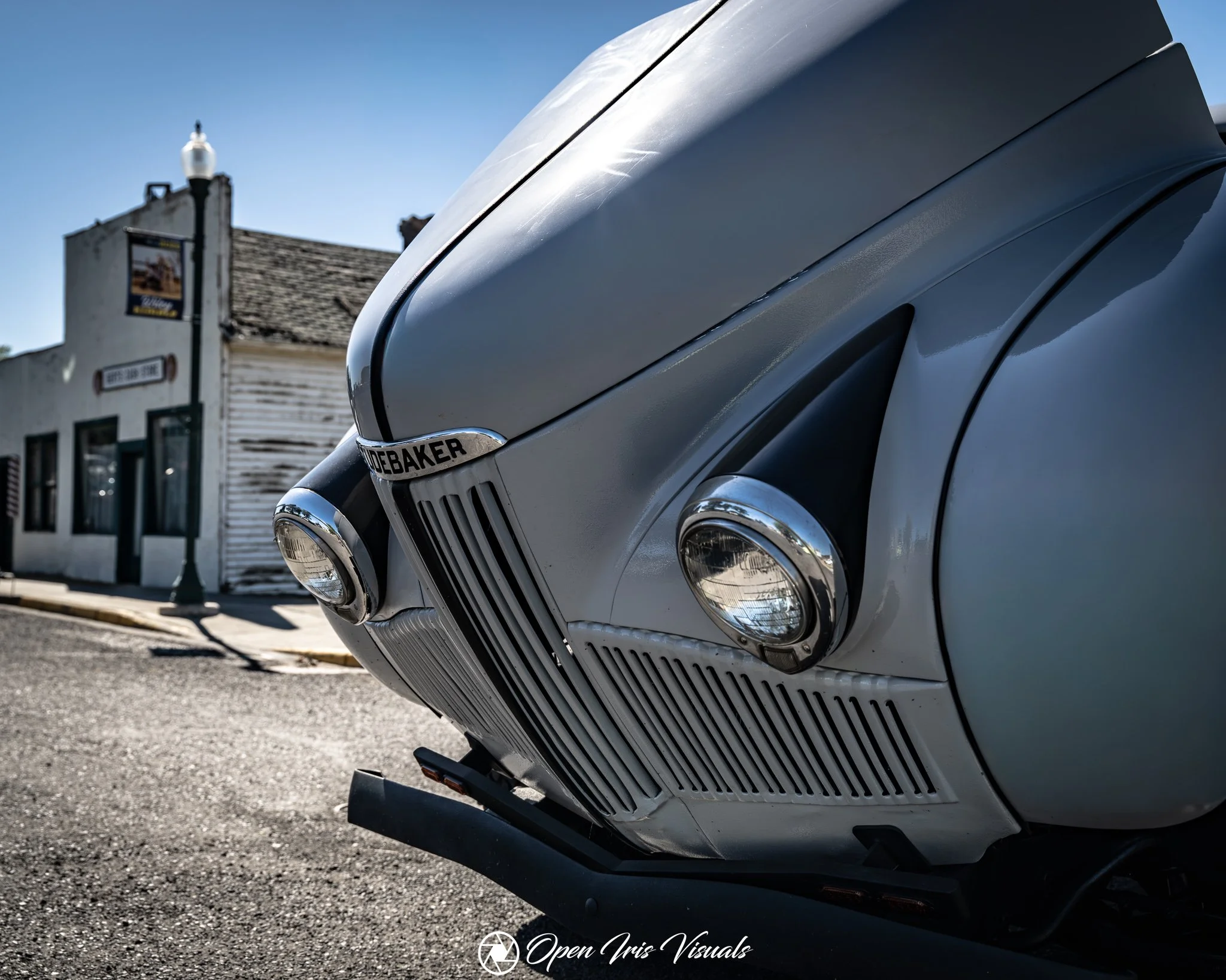 Close-up view of the front of a vintage silver Mercedes-Benz car parked on the street with a building and lamppost in the background.