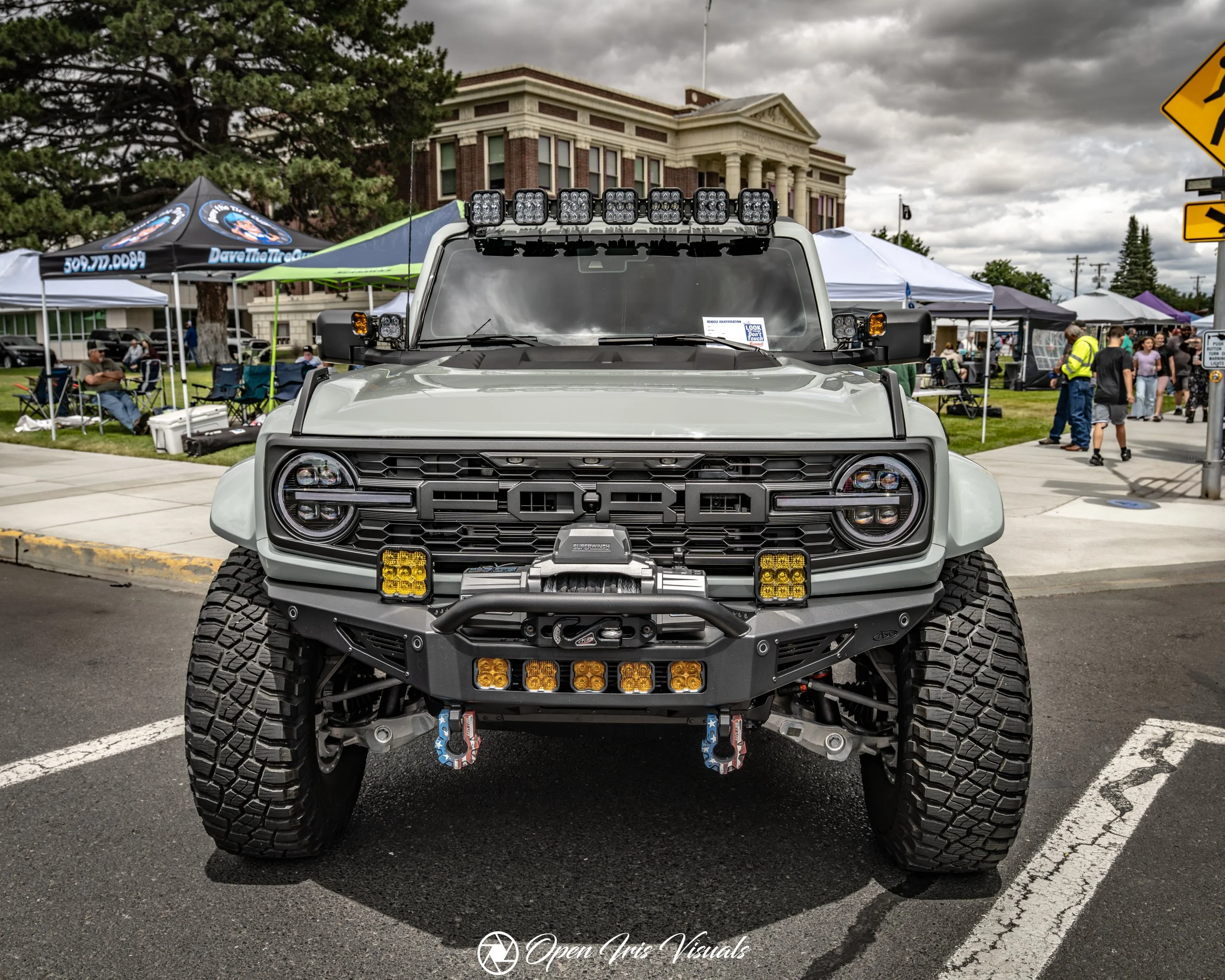 Front view of a customized off-road vehicle with large tires, LED lights, and a rugged bumper at an outdoor event