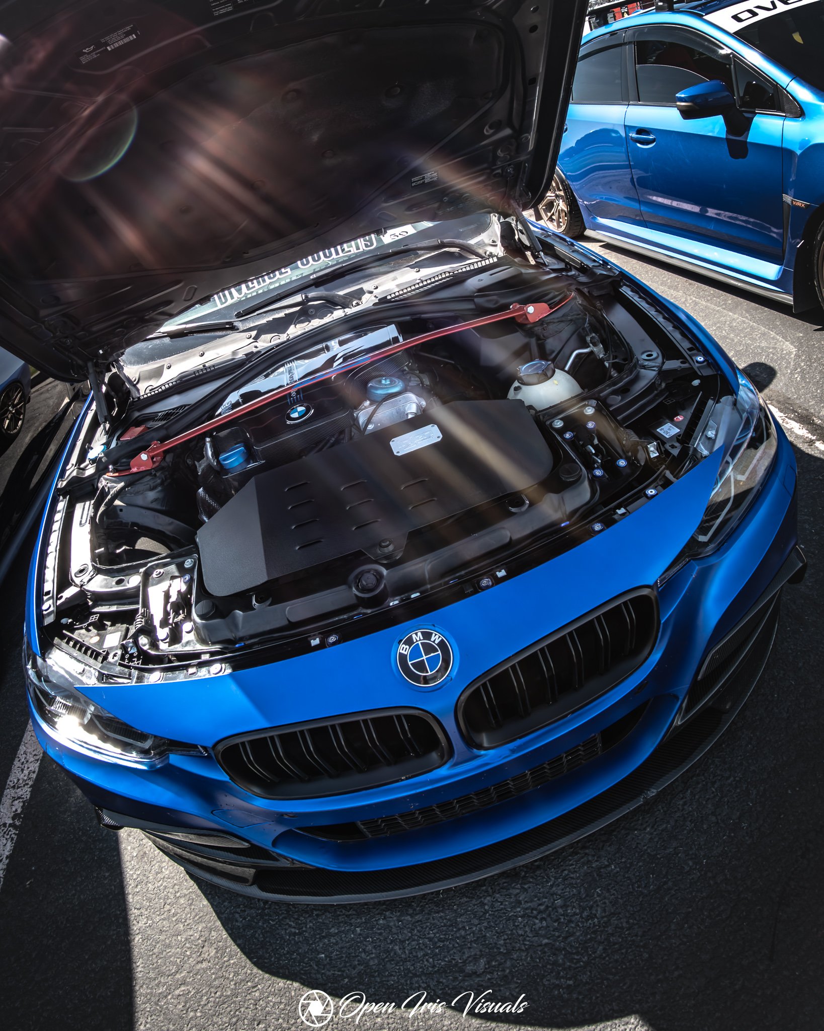 Blue BMW with open hood revealing engine bay during a local car show
