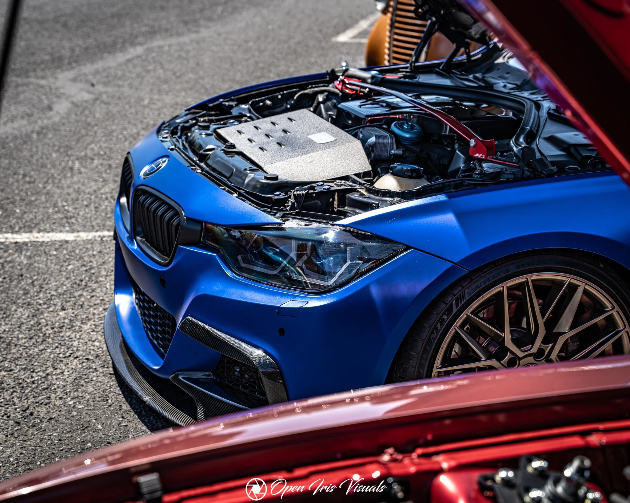 Blue BMW with its hood open, showing the engine bay with modifications, parked on an asphalt surface.