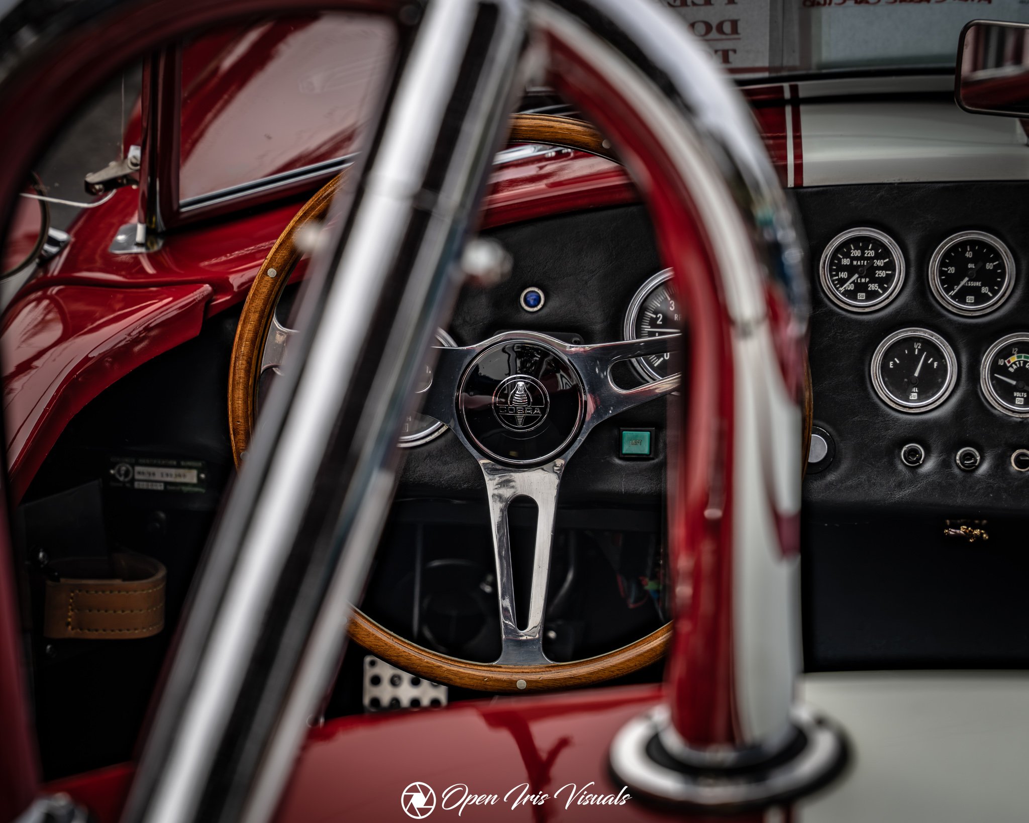 Close-up of the interior of a vintage car, featuring a wooden steering wheel, dashboard gauges, and red metal body panels.