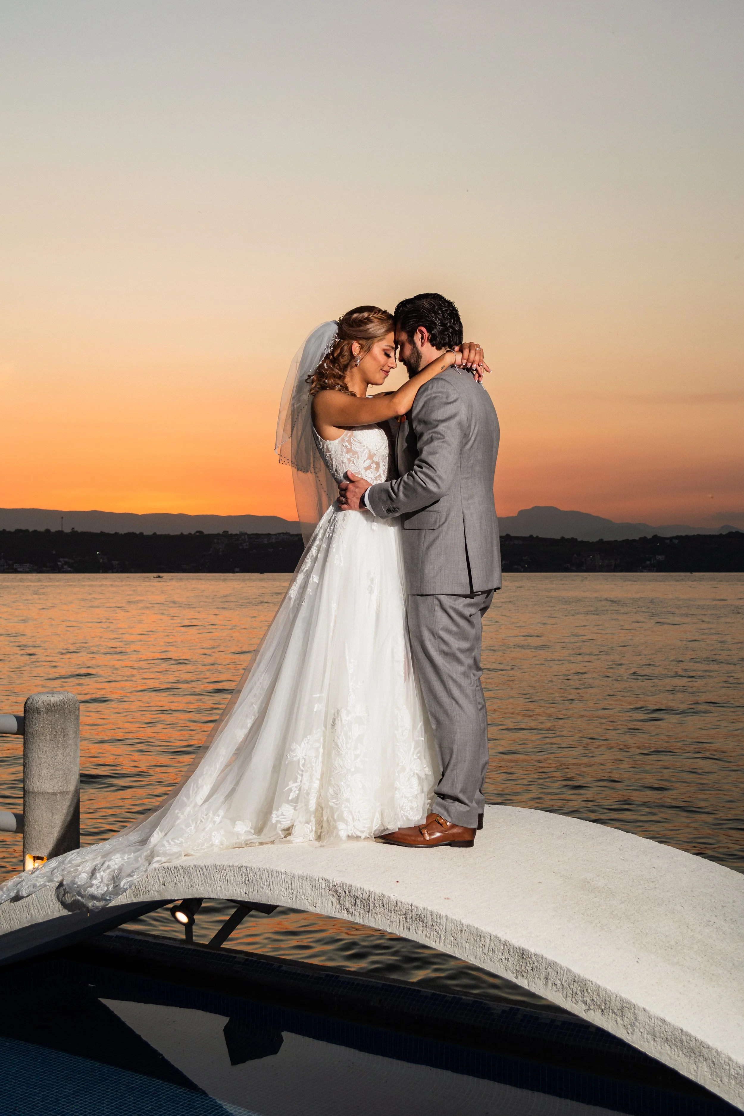 Pareja de novios en un abrazo íntimo, con el lago y montañas de fondo.