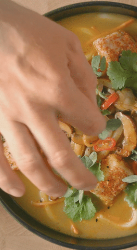 Hand adding cilantro to a bowl of vegetable soup with croutons.
