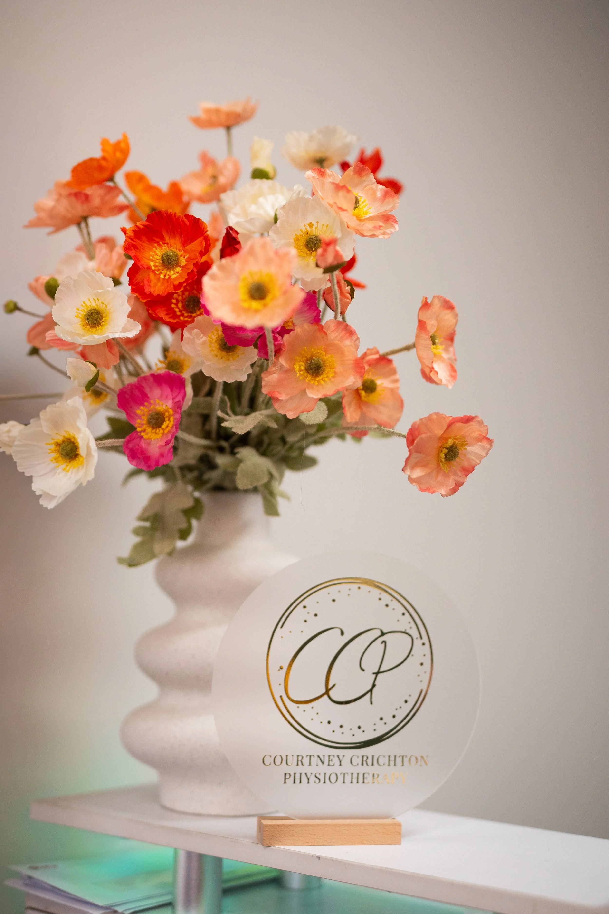 A bouquet of colorful flowers in a white vase next to a sign for Courtney Crichton Physiotherapy.