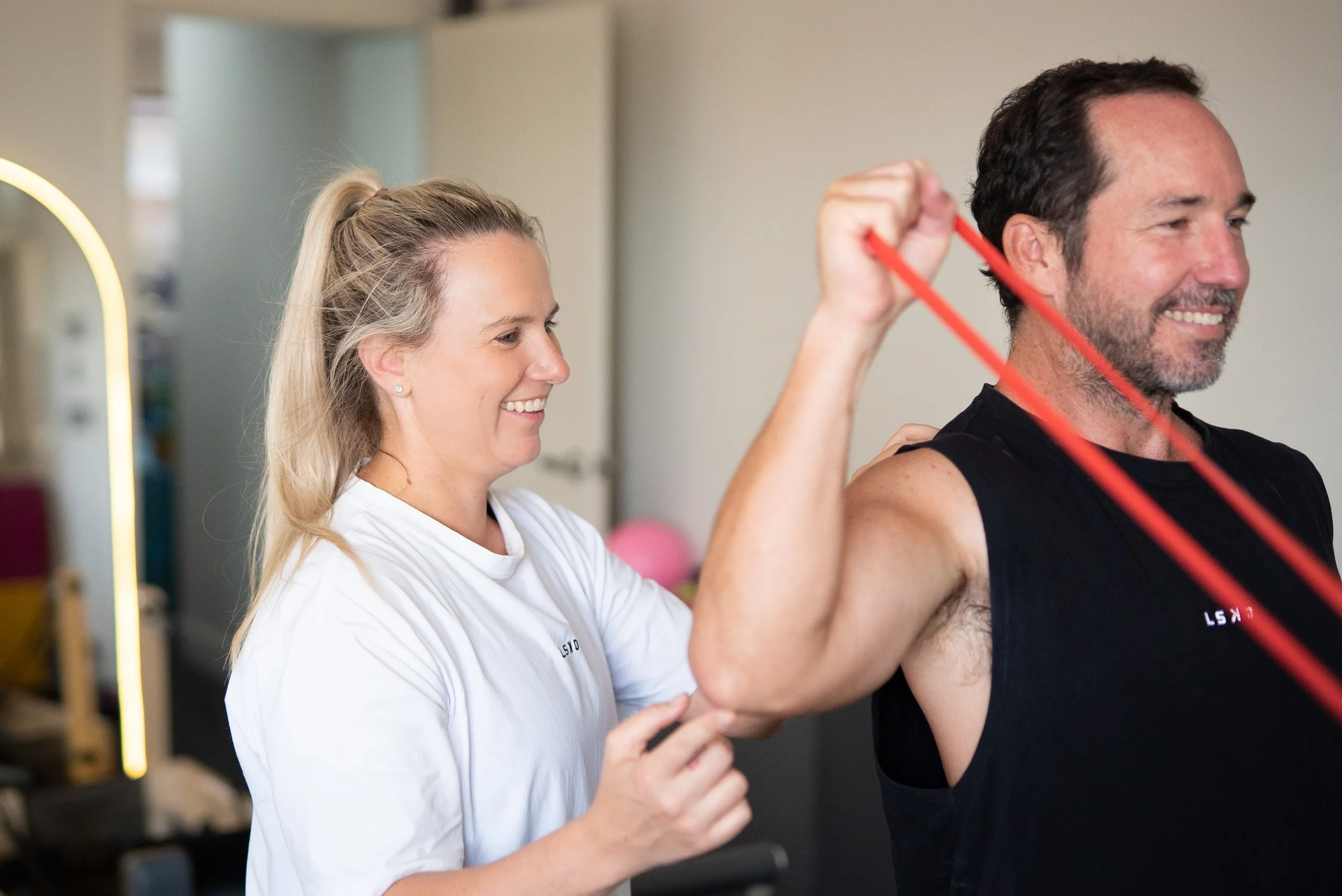 A woman trainer assisting a man during a fitness workout with resistance bands in a gym.