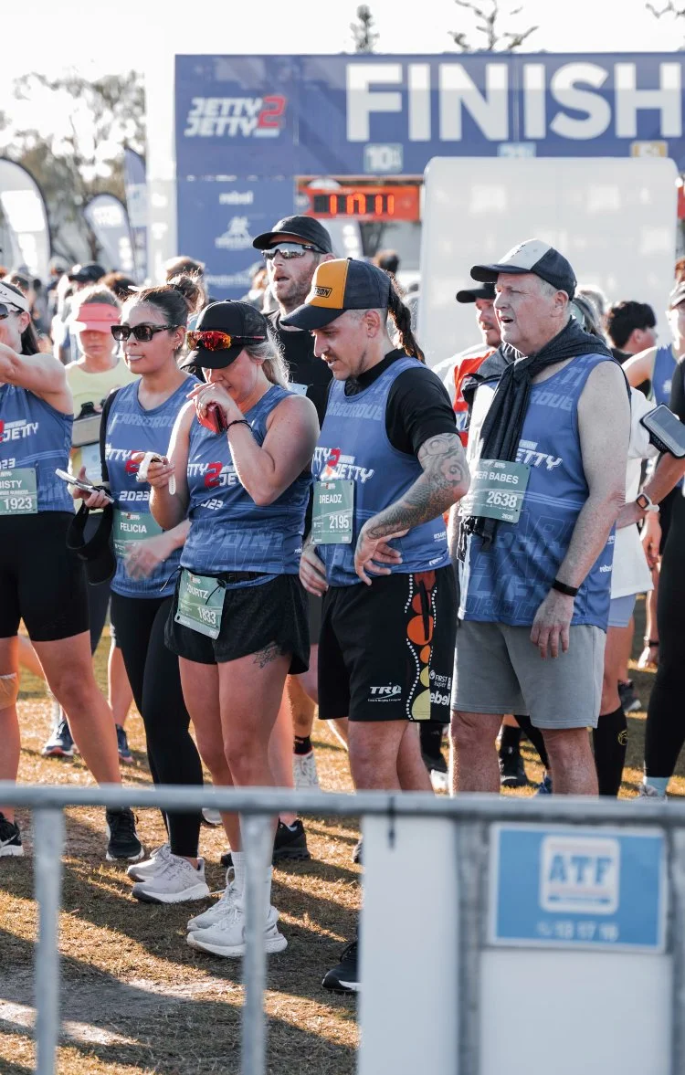 People standing at the finish line of a race event, with a large blue banner reading 'FINISH' in the background.