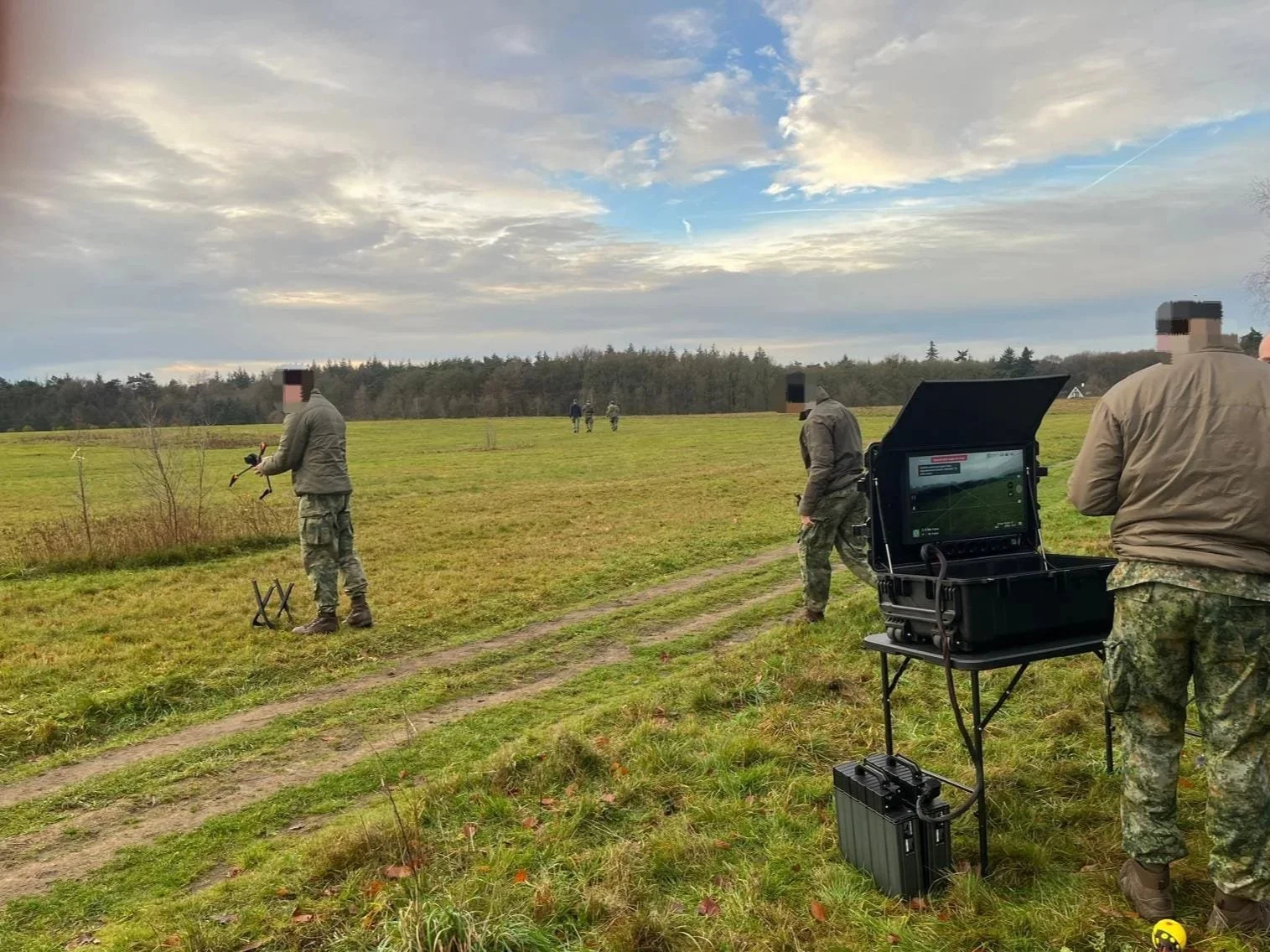 Military personnel operating equipment in an open field with a cloudy sky.