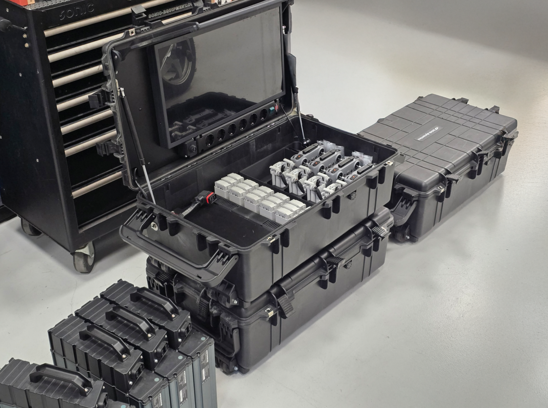 Open black equipment case containing multiple cameras and accessories on a light-colored floor.