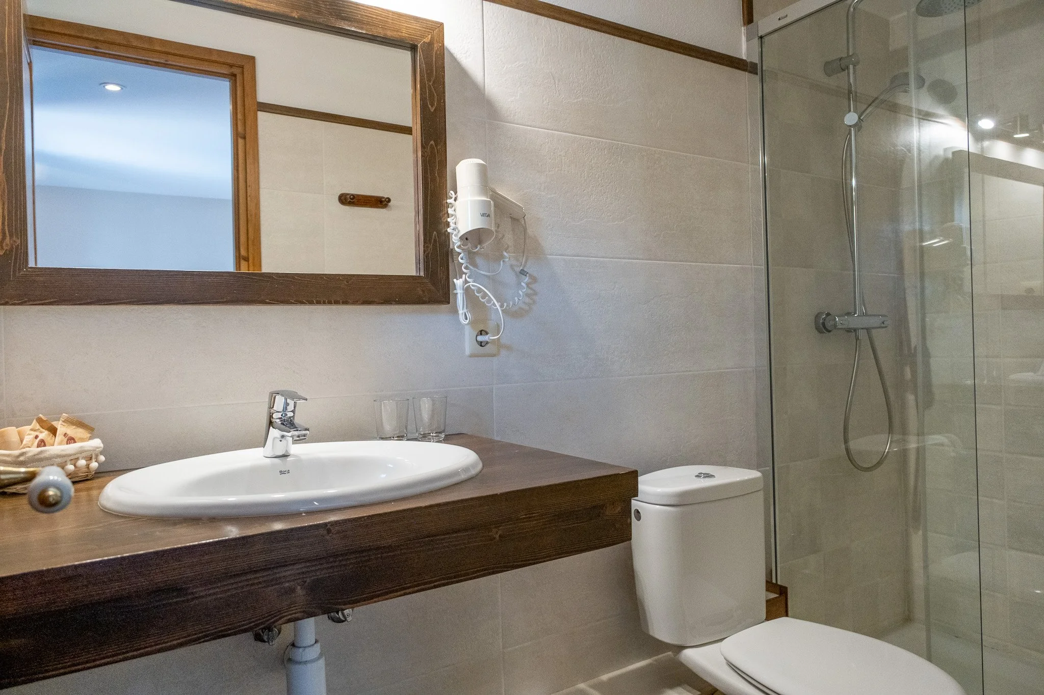Baño con lavabo, espejo, secador de cabello y ducha con puerta de vidrio