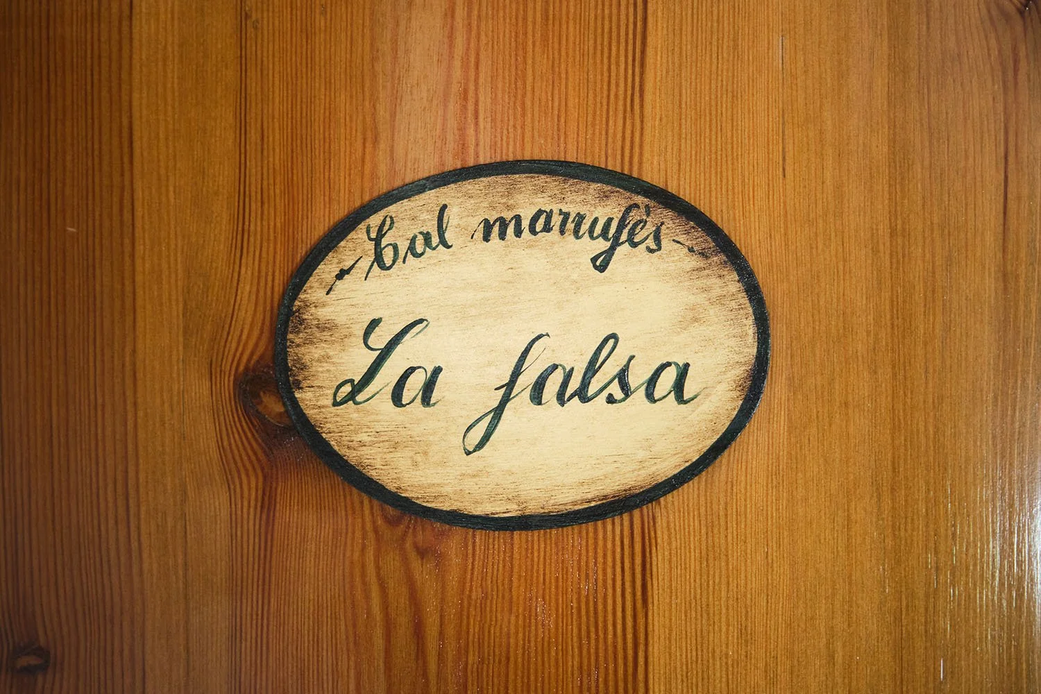 Cartel en madera con la inscripción "Cal Marrufès, La falsa" en letra cursiva, en una pared de madera.
