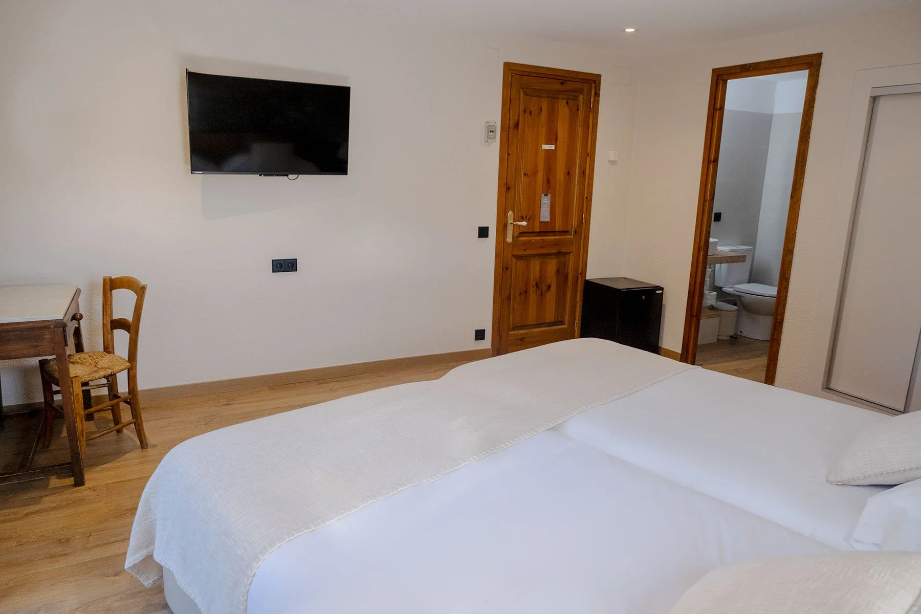 Habitación de hotel con cama, televisión, escritorio y baño visible a través de una puerta