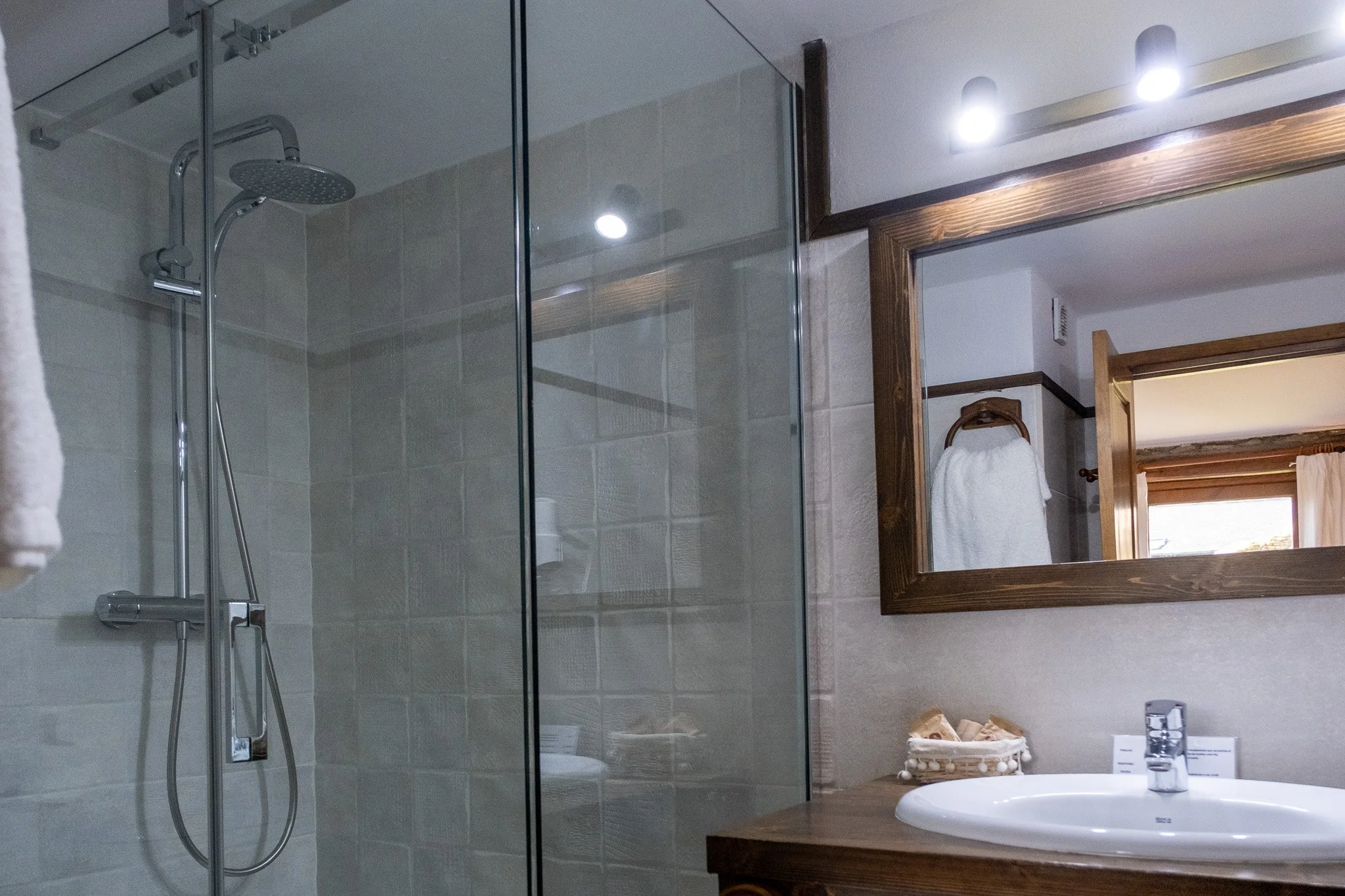 Baño con ducha de cristal, lavabo y espejo de madera.