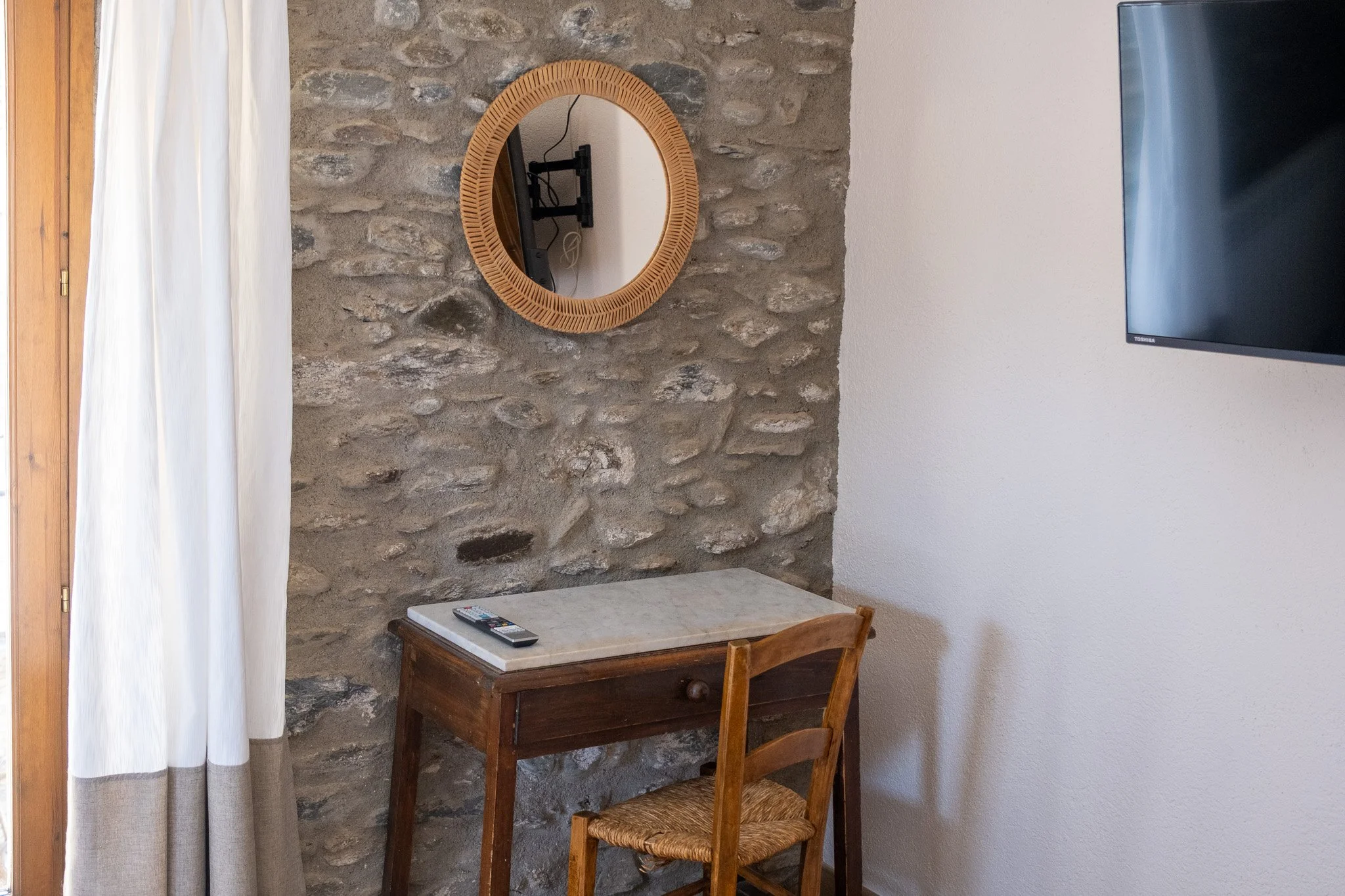 Escritorio con una silla de madera, una televisión en la pared y un espejo redondo en la pared de piedra.