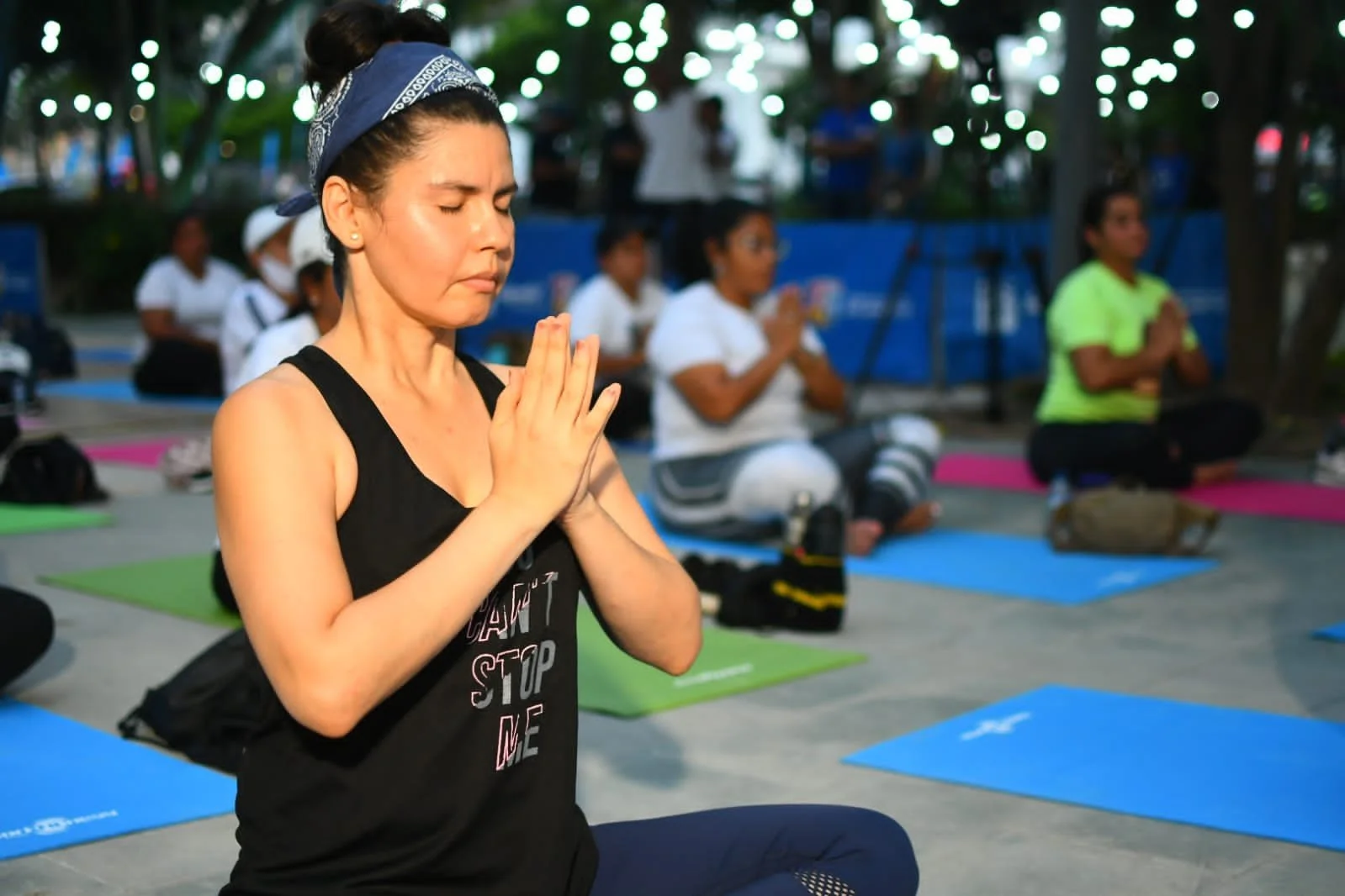 Mujer practicando yoga en grupo, en posición de oración, durante una clase al aire libre.