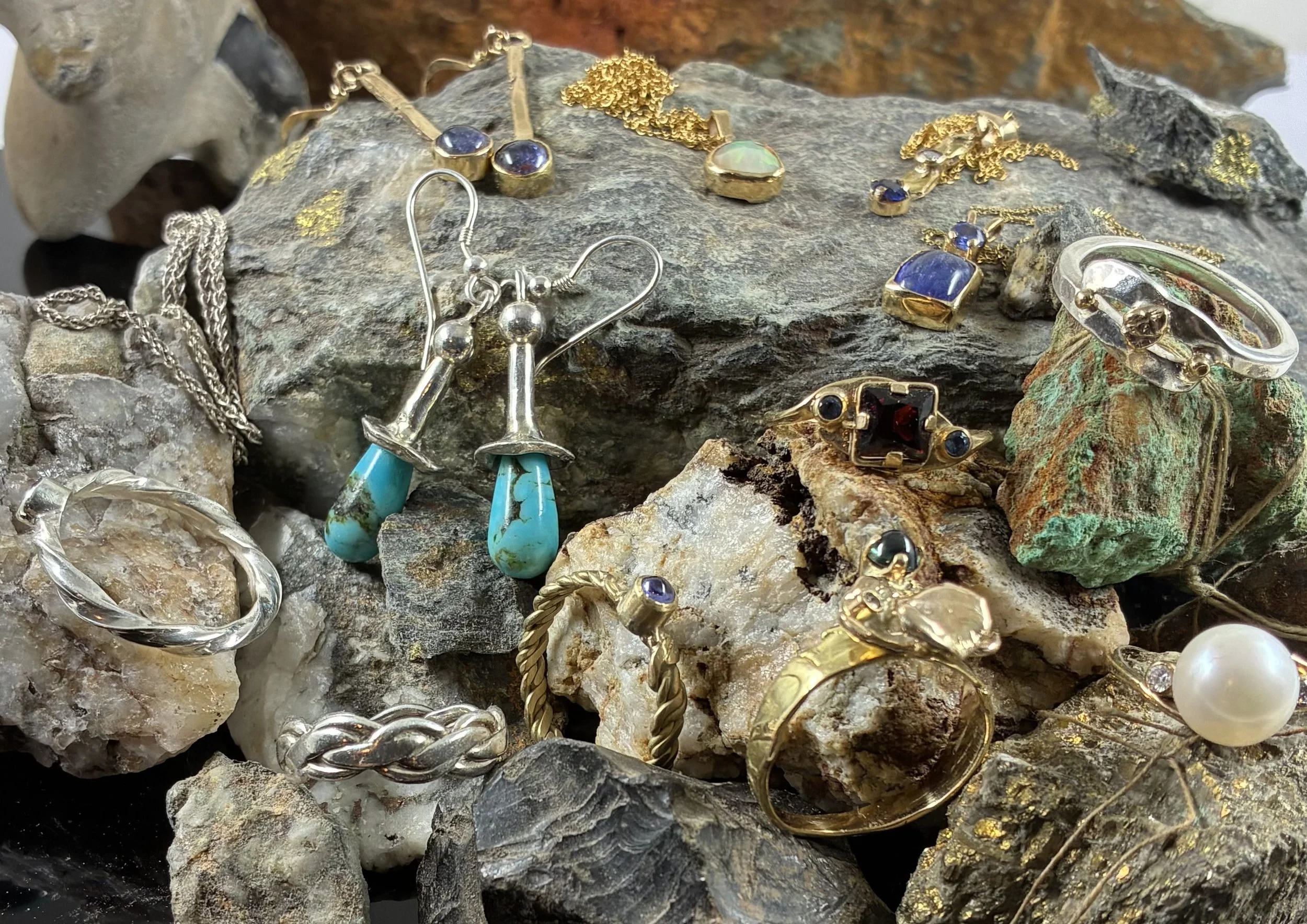 Various jewelry pieces, including rings, necklaces, earrings, and rings with gemstones, displayed on rocks and mineral stones.