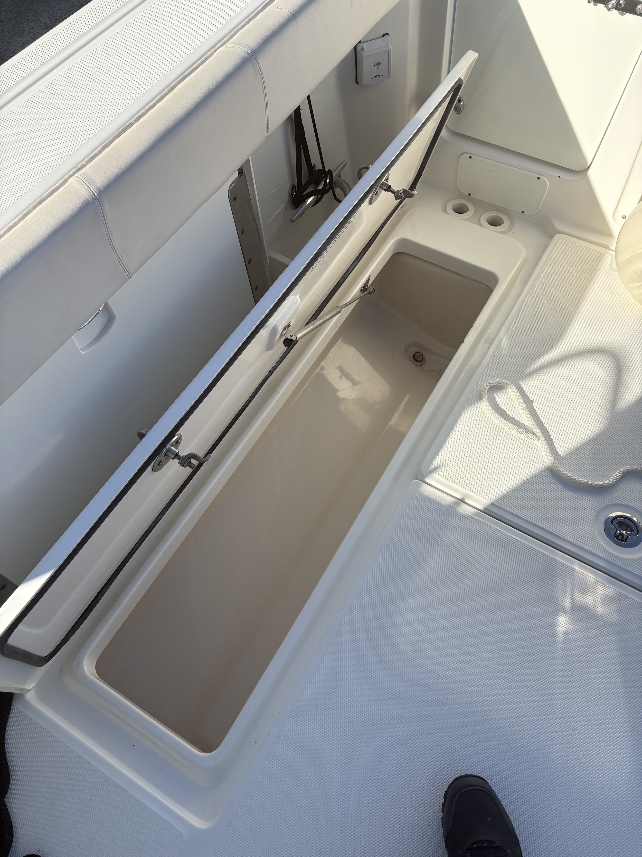 Empty insulated fish storage compartment on a boat with a hatch cover propped open and a railing above it.