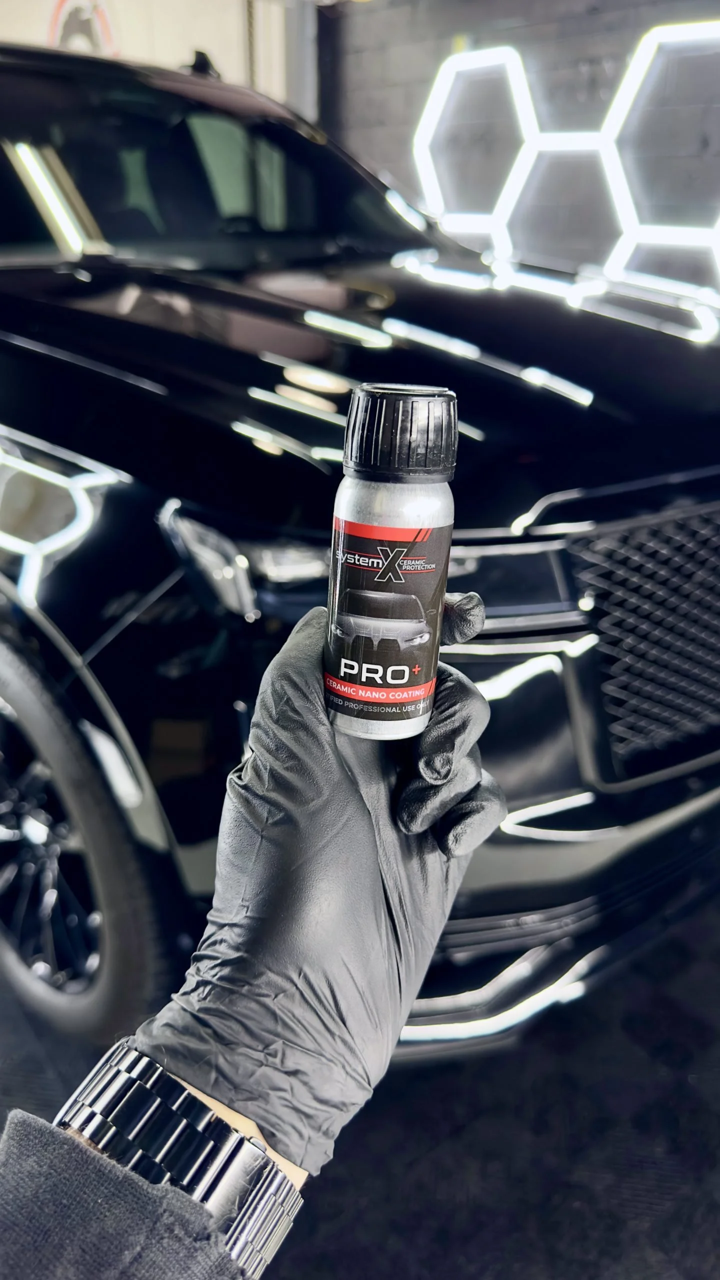 System X Installer holding a ceramic coating bottle with a black ceramic coated car in the back