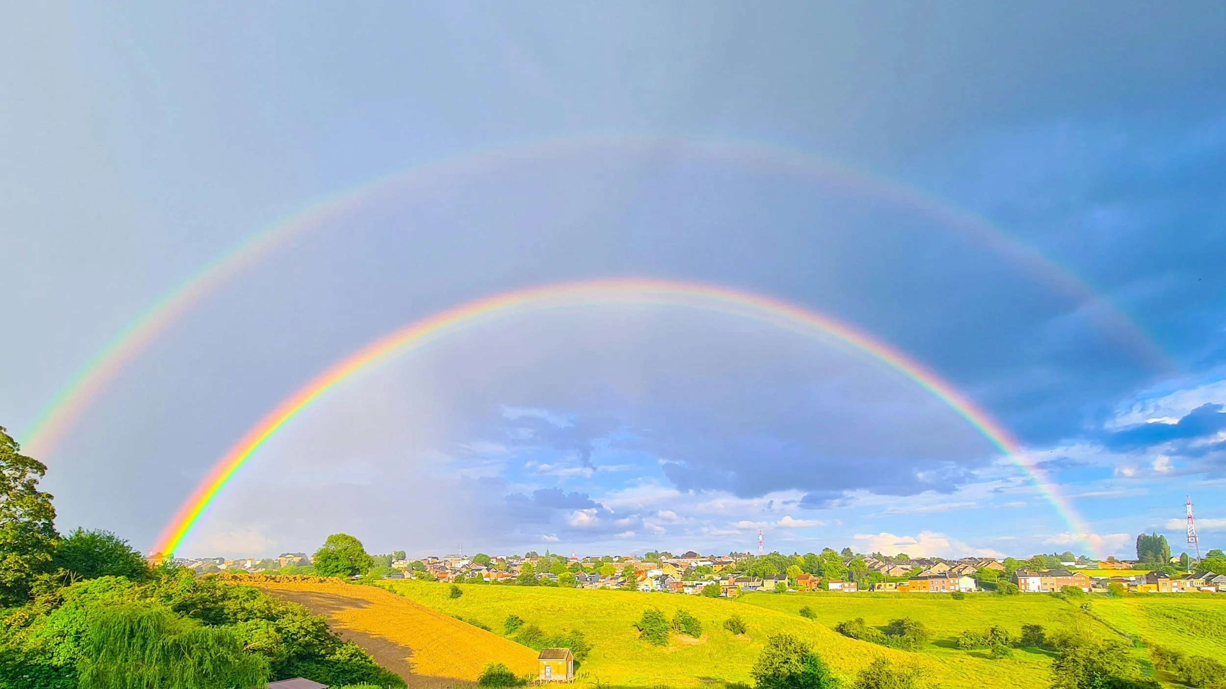 Double Rainbow in a bright blue sky over a green field