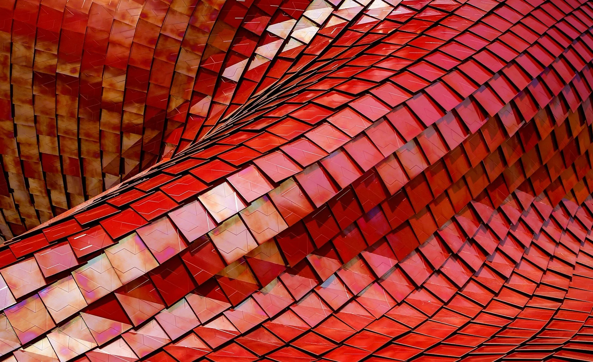 Close-up of an architectural structure with red, orange, and pink reflective tiles arranged in a flowing, curved pattern.