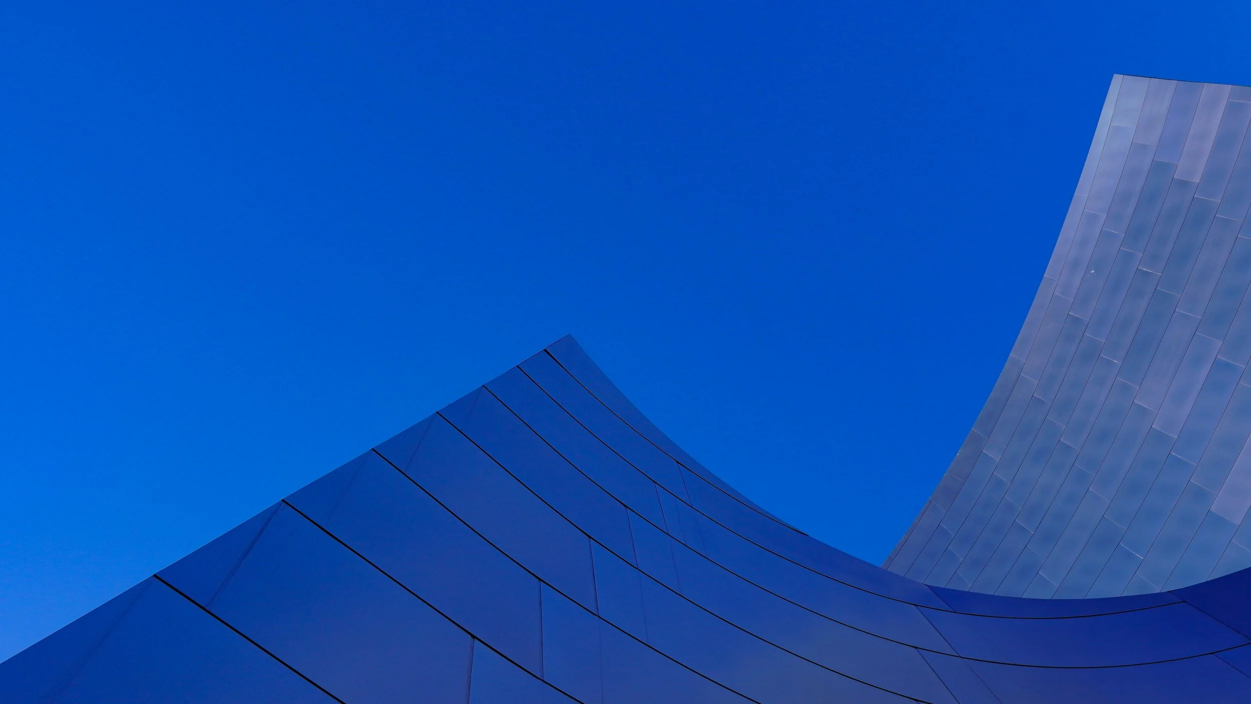 Modern building with curved and angular metallic surface against a clear blue sky.