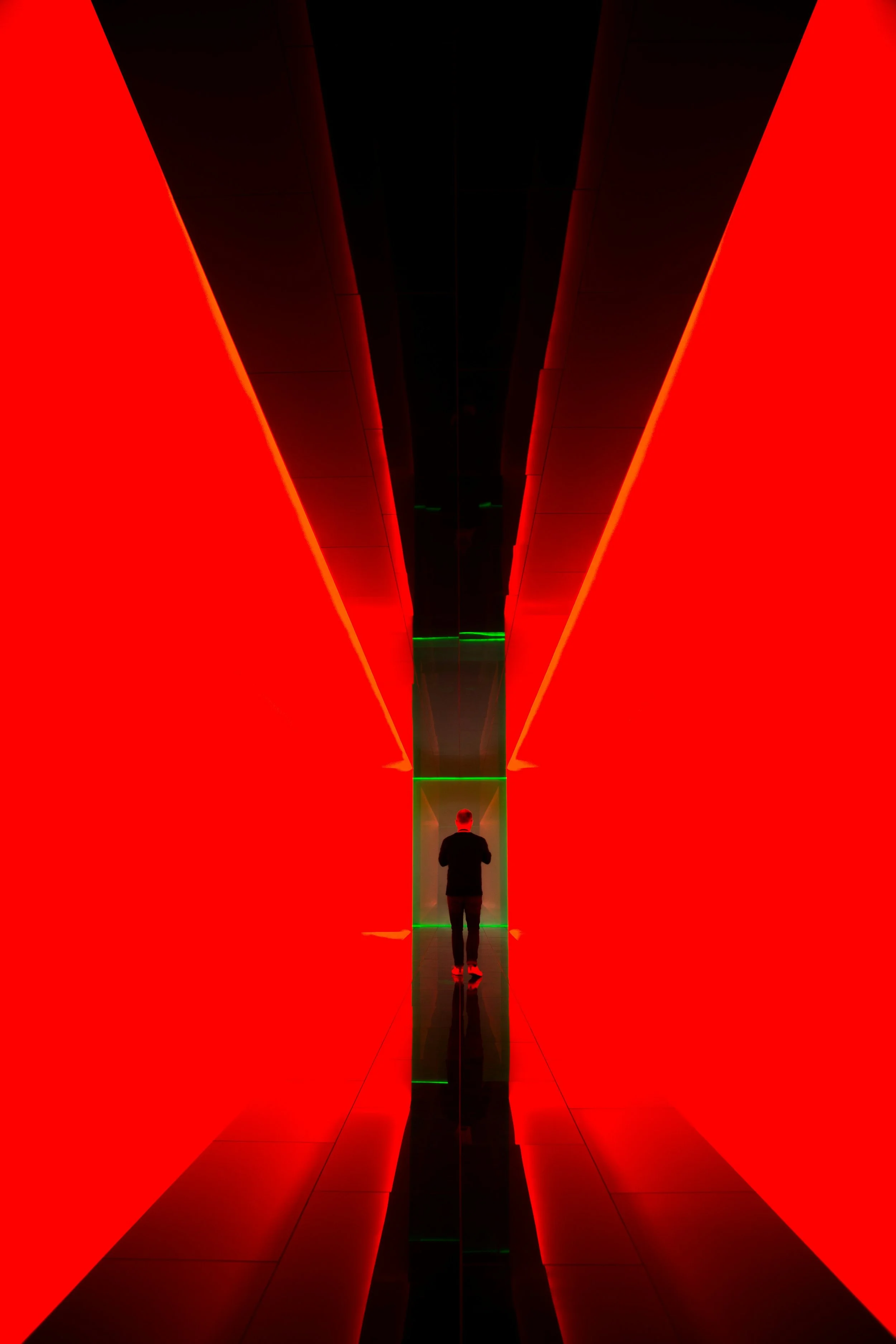 A person walking through a futuristic tunnel with red and black walls and green accent lighting.