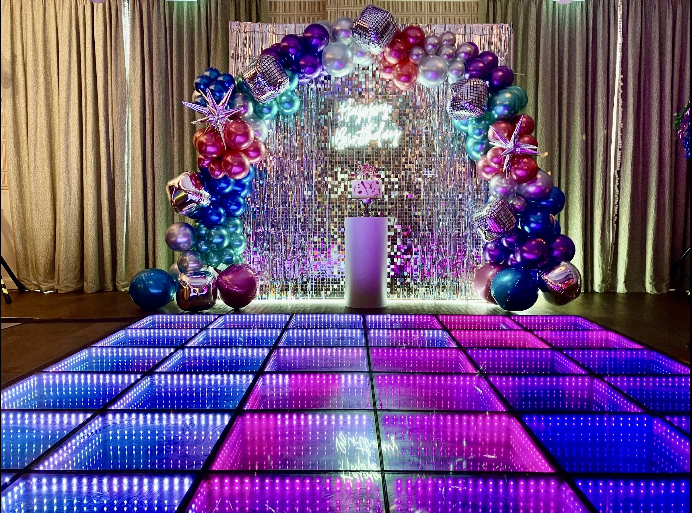 Colorful graffiti wall with abstract designs and words, a vibrant dance floor with pink, purple, blue, green, yellow, and orange sections, and a large illuminated number 6 with small lights. Confetti is scattered on the dance floor and floor in front of it.