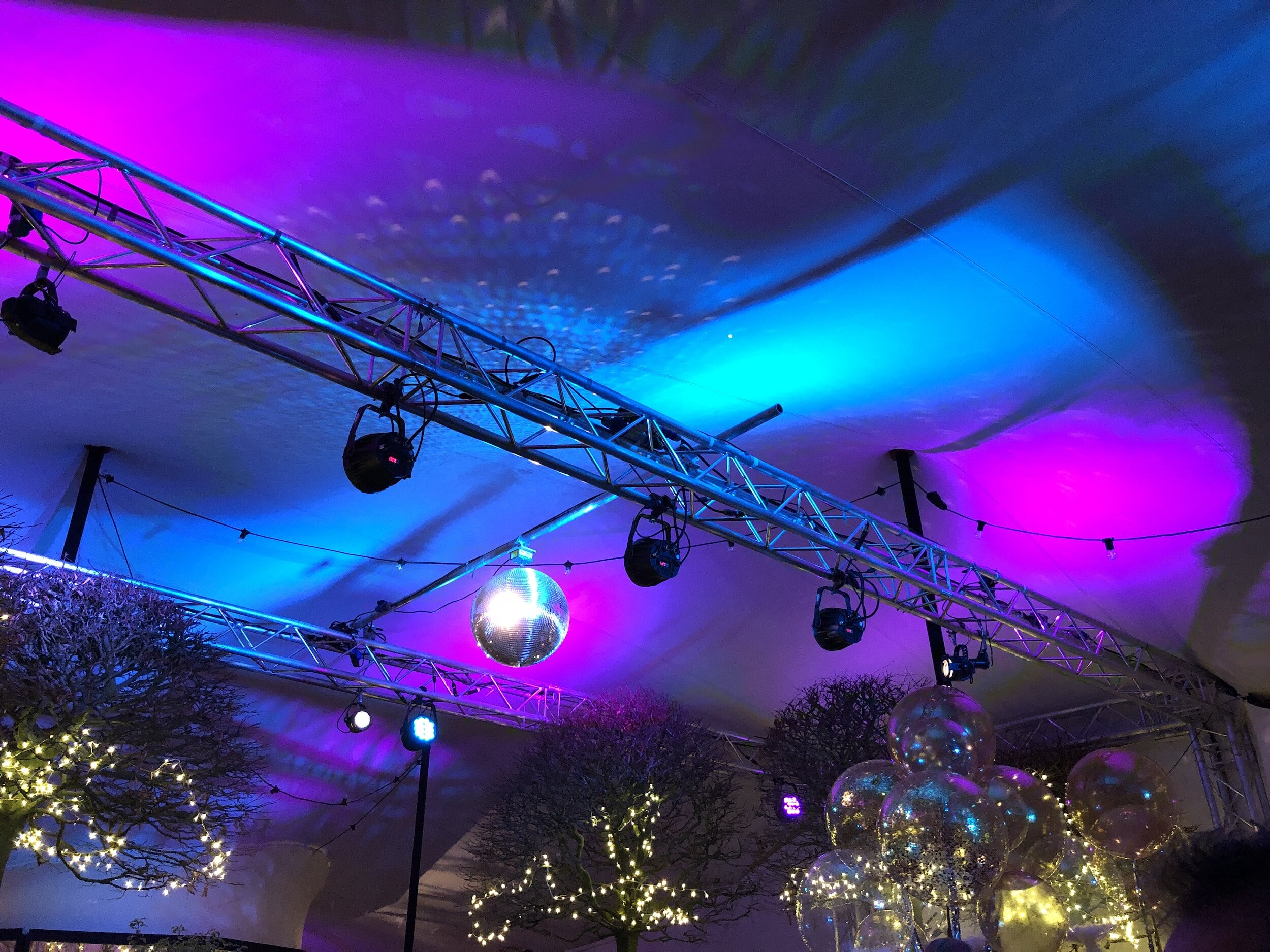 Decorated indoor space with purple and blue lighting, disco balls, and illuminated trees.
