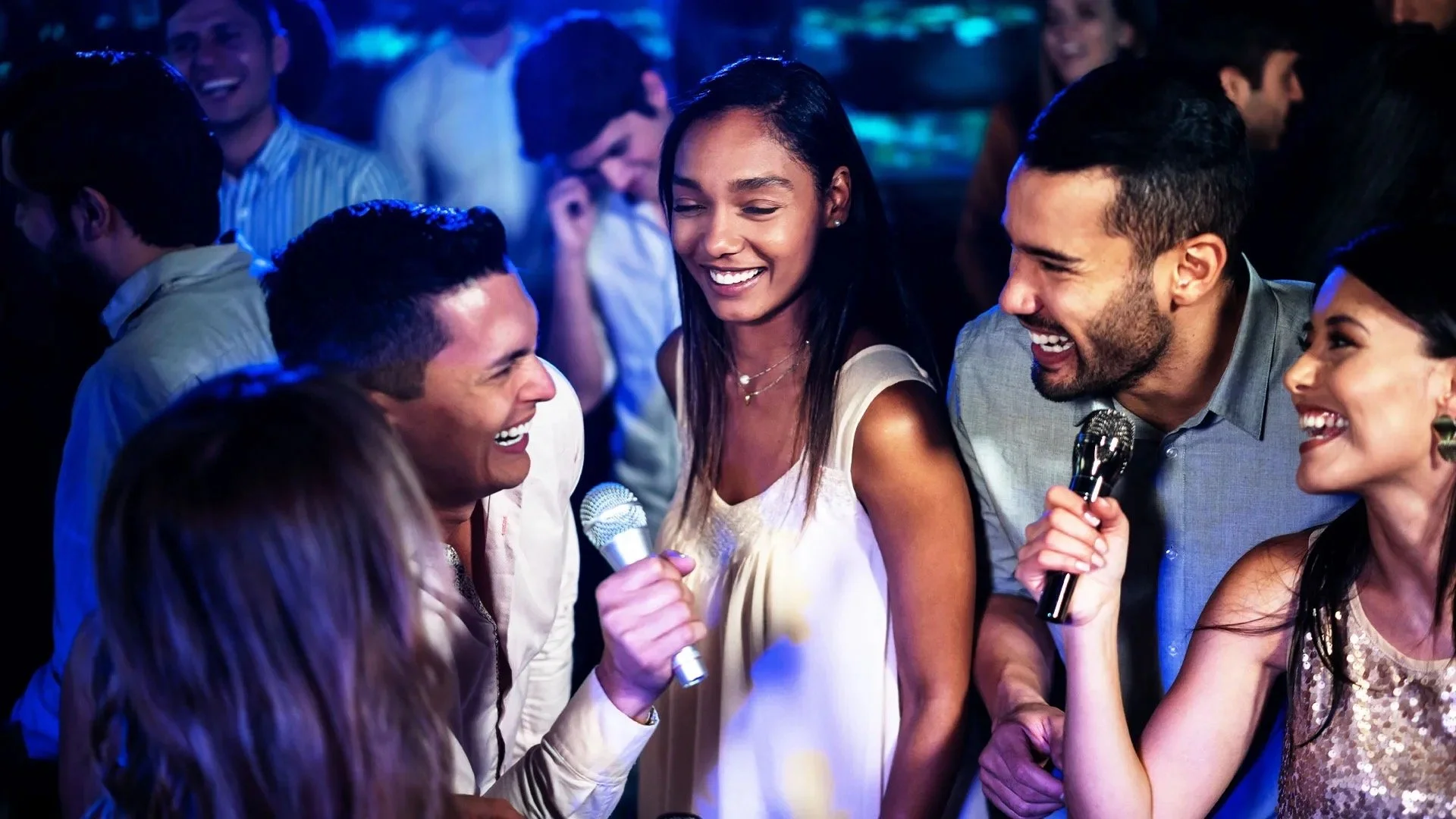 Group of people singing and having fun at a karaoke night, holding microphones, smiling, and laughing.