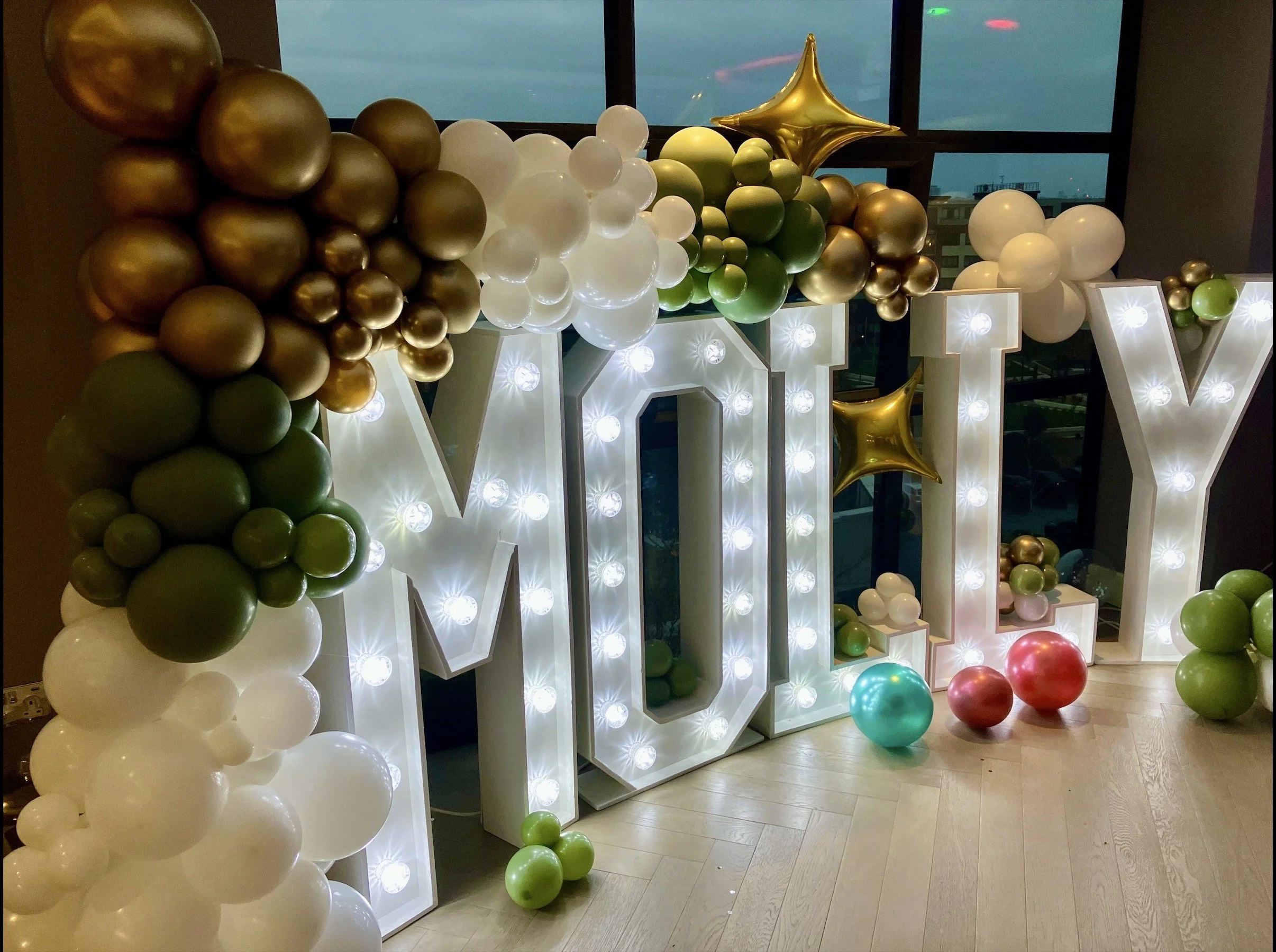 Interior of a grand hall with large arched window, two statues, palm trees, a DJ booth, and floral arrangements.