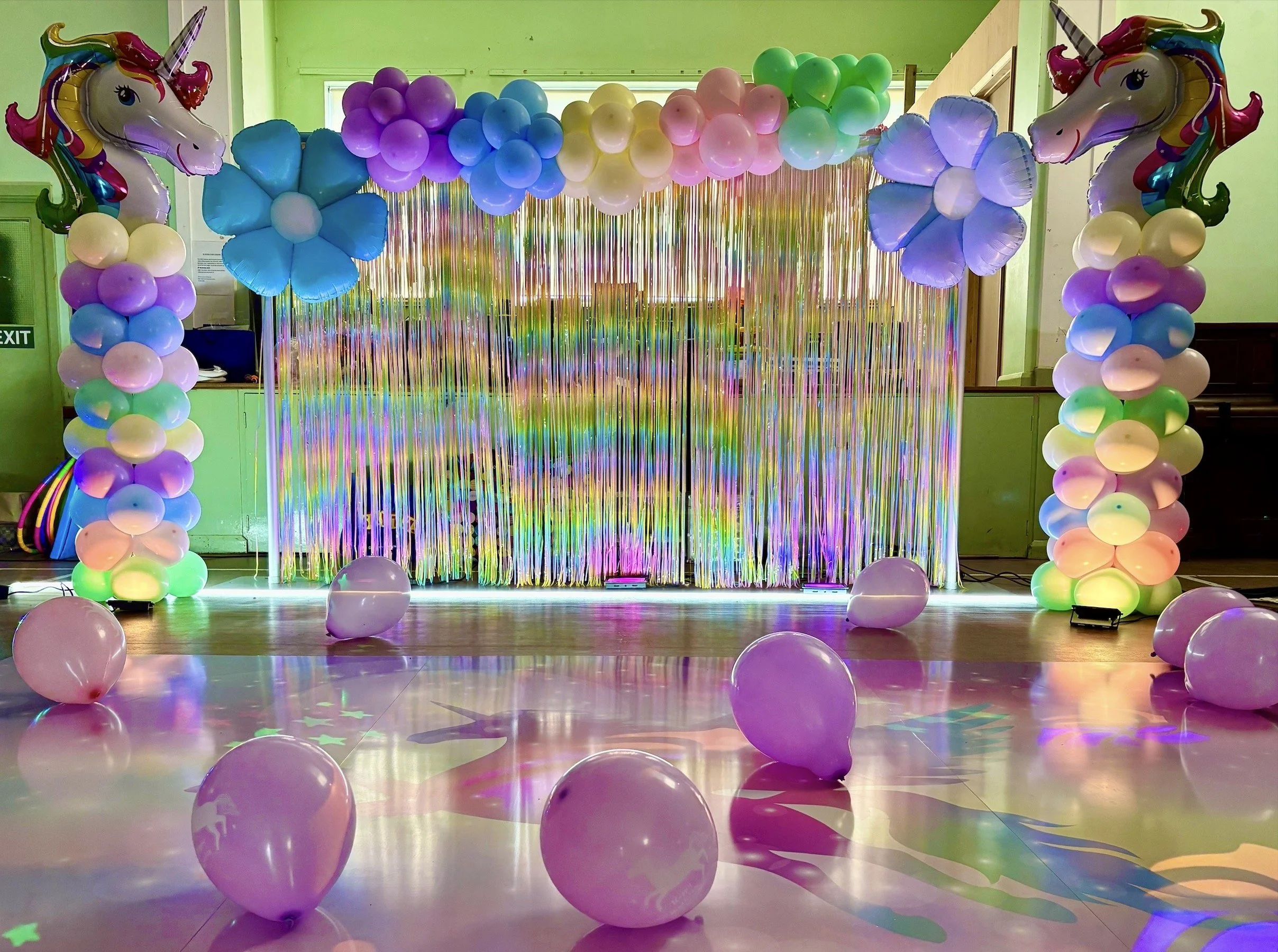 Black and white photo of a woman and a man facing each other with a vintage microphone in between, woman wearing a sequined dress and the man wearing a hat, in front of a curtain with lights.
