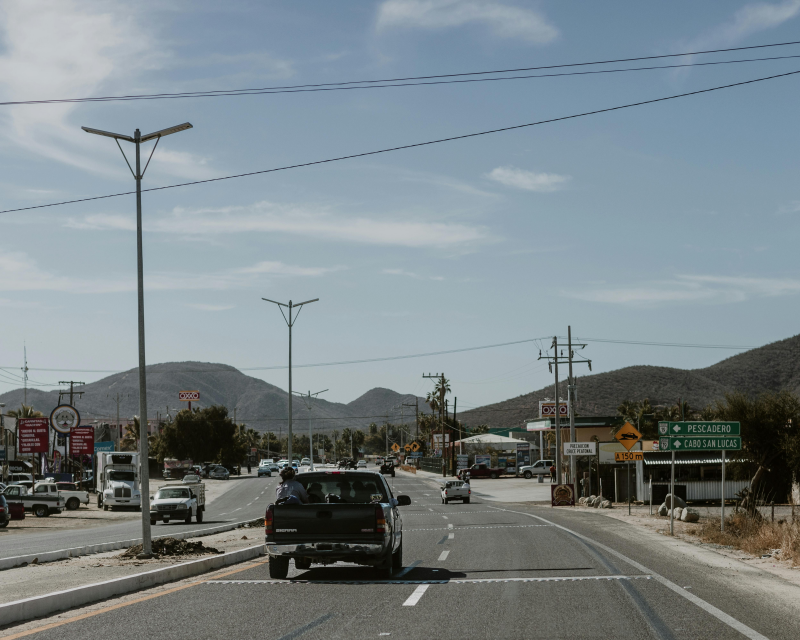 A small town street scene with light traffic, streetlights, and distant hills.