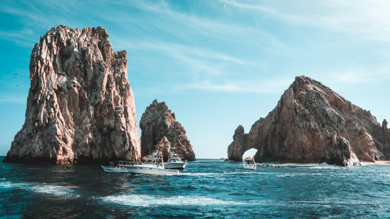 Boats sailing between large rocky islands in the ocean under a partly cloudy sky.