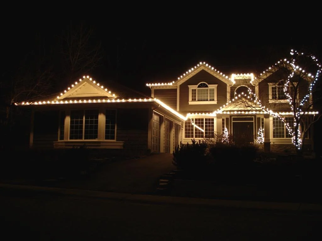 Warm white C9 Christmas lights installed along residential roofline in Calgary with additional tree lighting accents