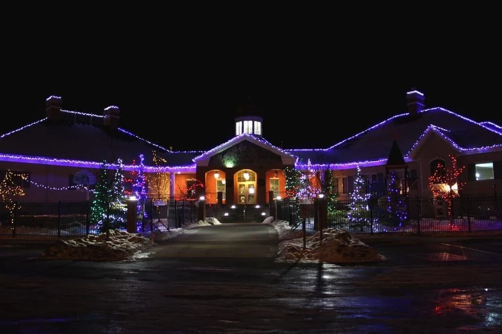 Large commercial holiday lighting installation at McKenzie Towne Community Centre in Calgary featuring multi-colour tree lighting and illuminated rooflines