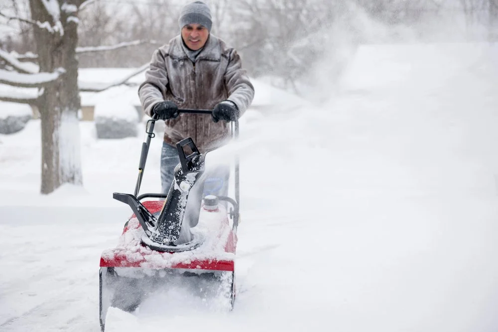 Residential snow removal in Calgary using a snowblower to clear a driveway during heavy snowfall